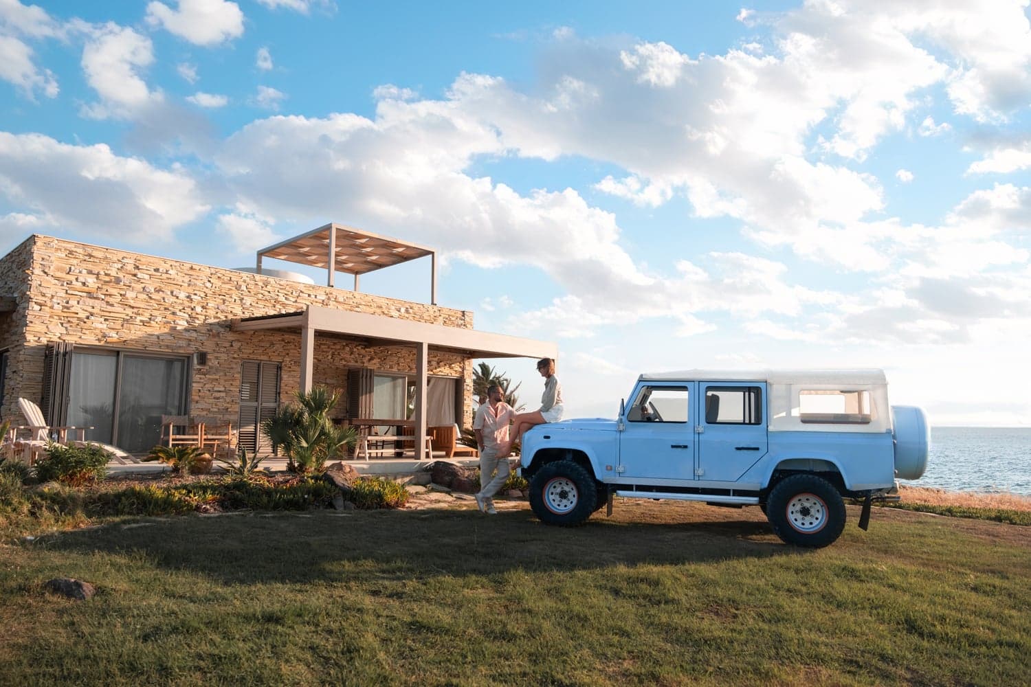 Monarch Defender custom Land Rover parked by a seaside home under a blue sky.