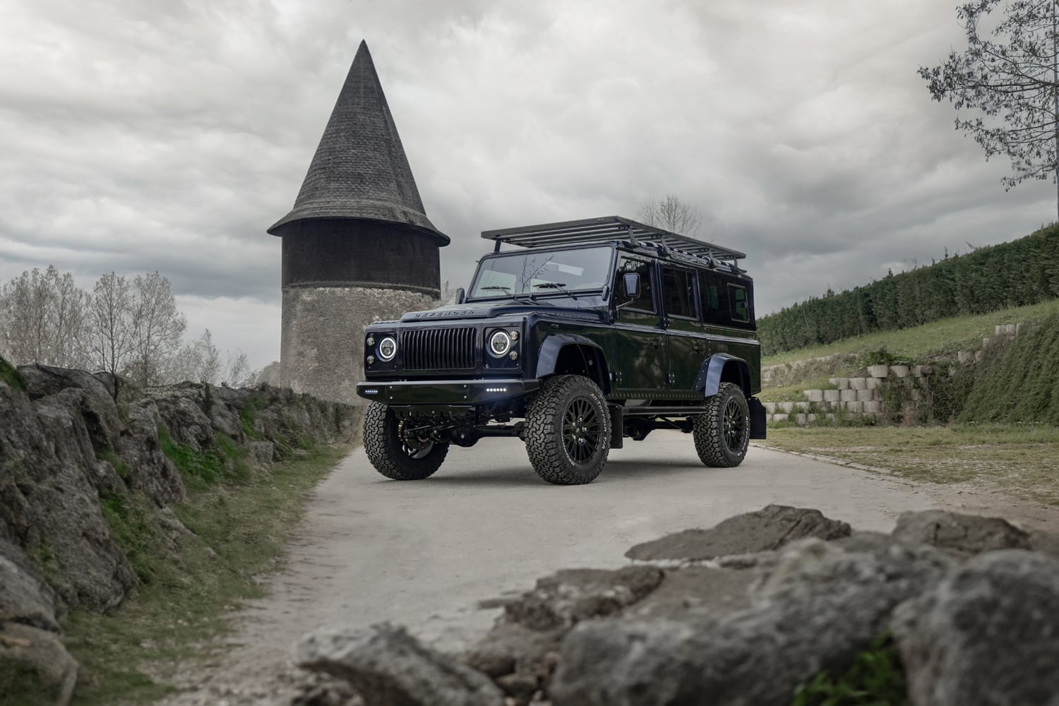Front View: Custom Land Rover Defender Modified Land Rover Defender parked on a gravel path near a historic tower