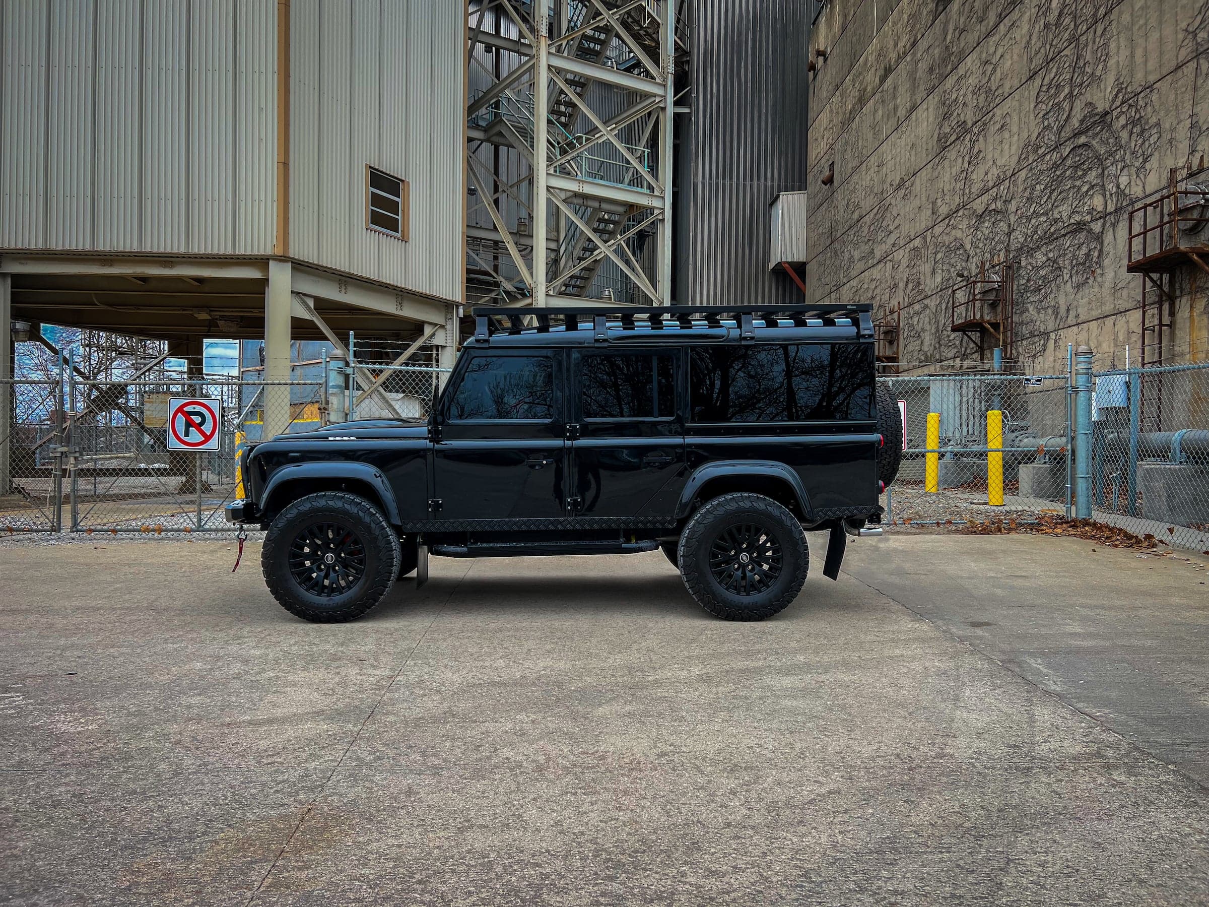 Side View: Custom Black Defender Black custom Land Rover Defender parked in an industrial setting