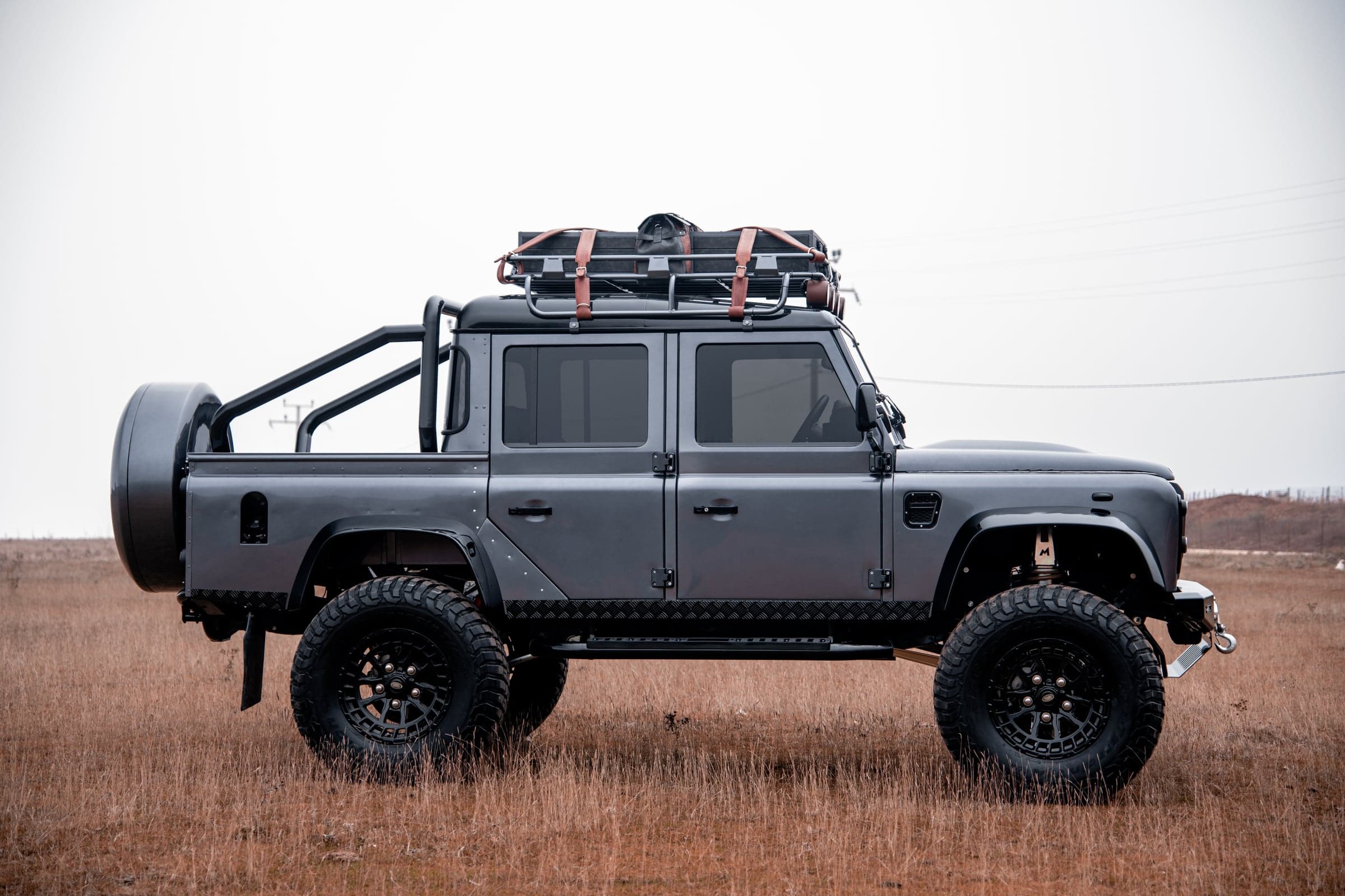 Side View: Bespoke Land Rover Defender Side view of a custom Land Rover Defender with off-road tires and rooftop storage