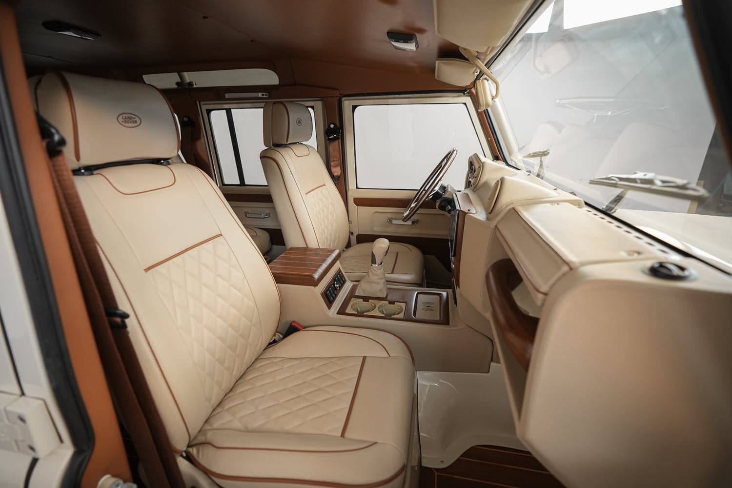 Interior Shot: Luxury Cabin Interior view of a bespoke Land Rover Defender featuring premium beige leather seats with brown accents and wood trim
