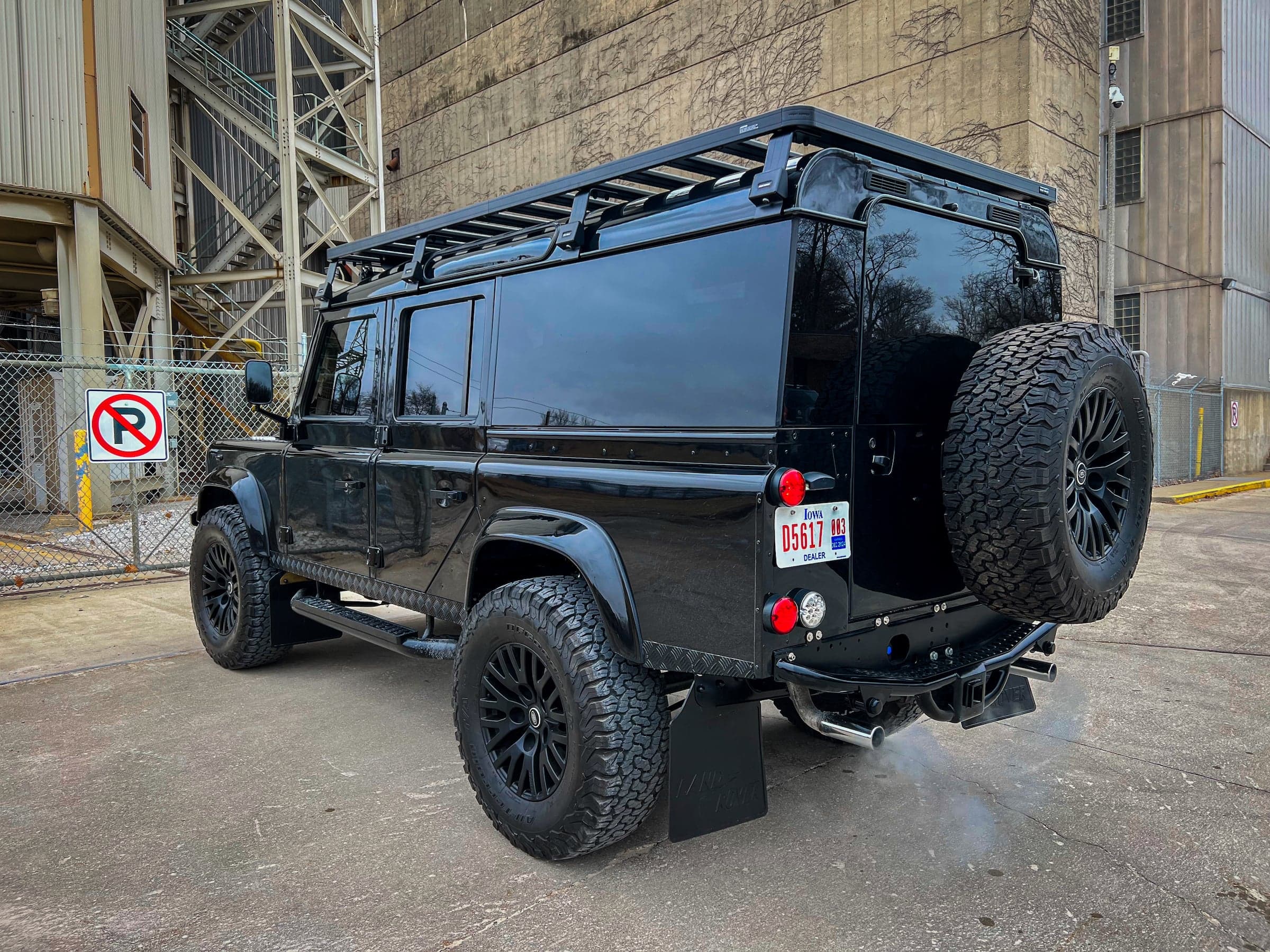 Rear View: Bespoke Land Rover Defender Black modified Land Rover Defender with off-road tires and roof rack