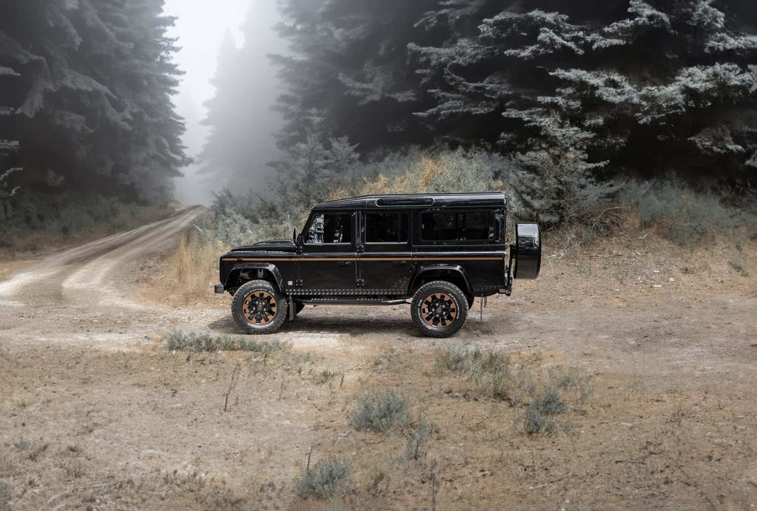 Custom Land Rover Defender parked on a dirt road in a misty forest