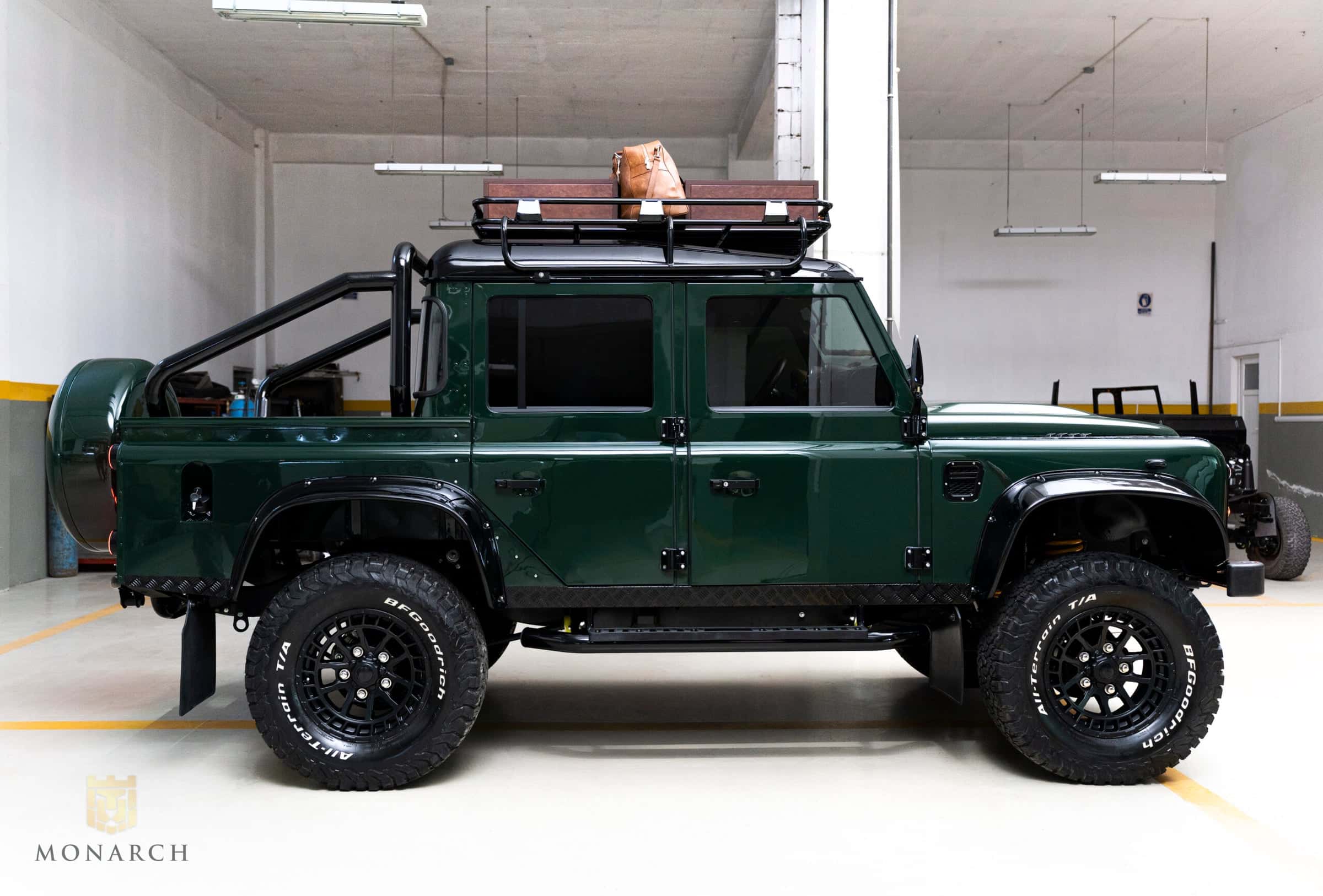 Side view of a custom green Land Rover Defender with off-road tires and roof rack