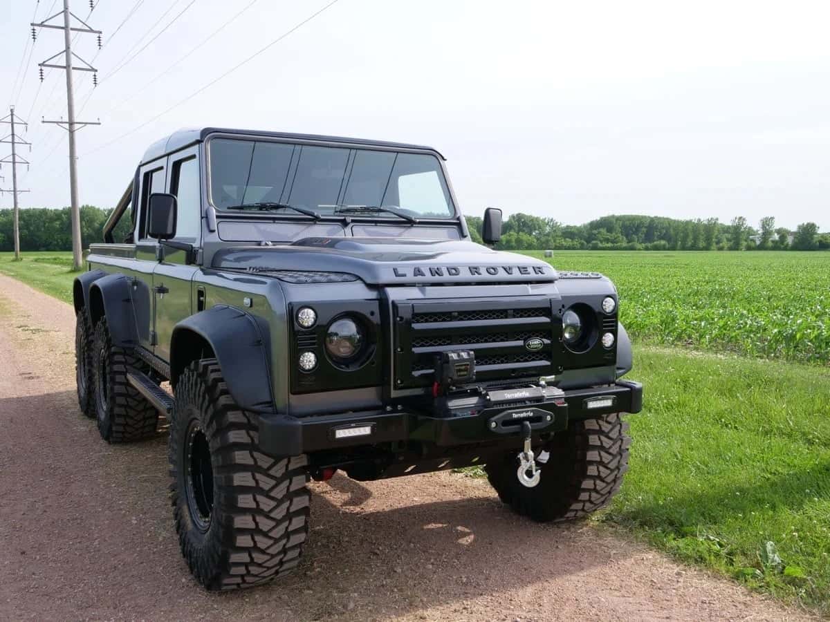 Black modified Land Rover Defender parked on a dirt road with lush green fields in the background