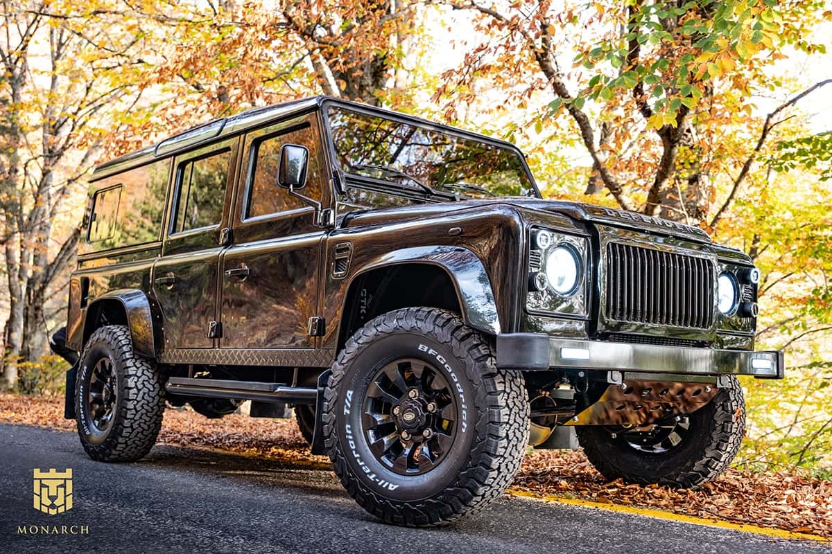 Custom black Land Rover Defender parked on a scenic road with autumn foliage