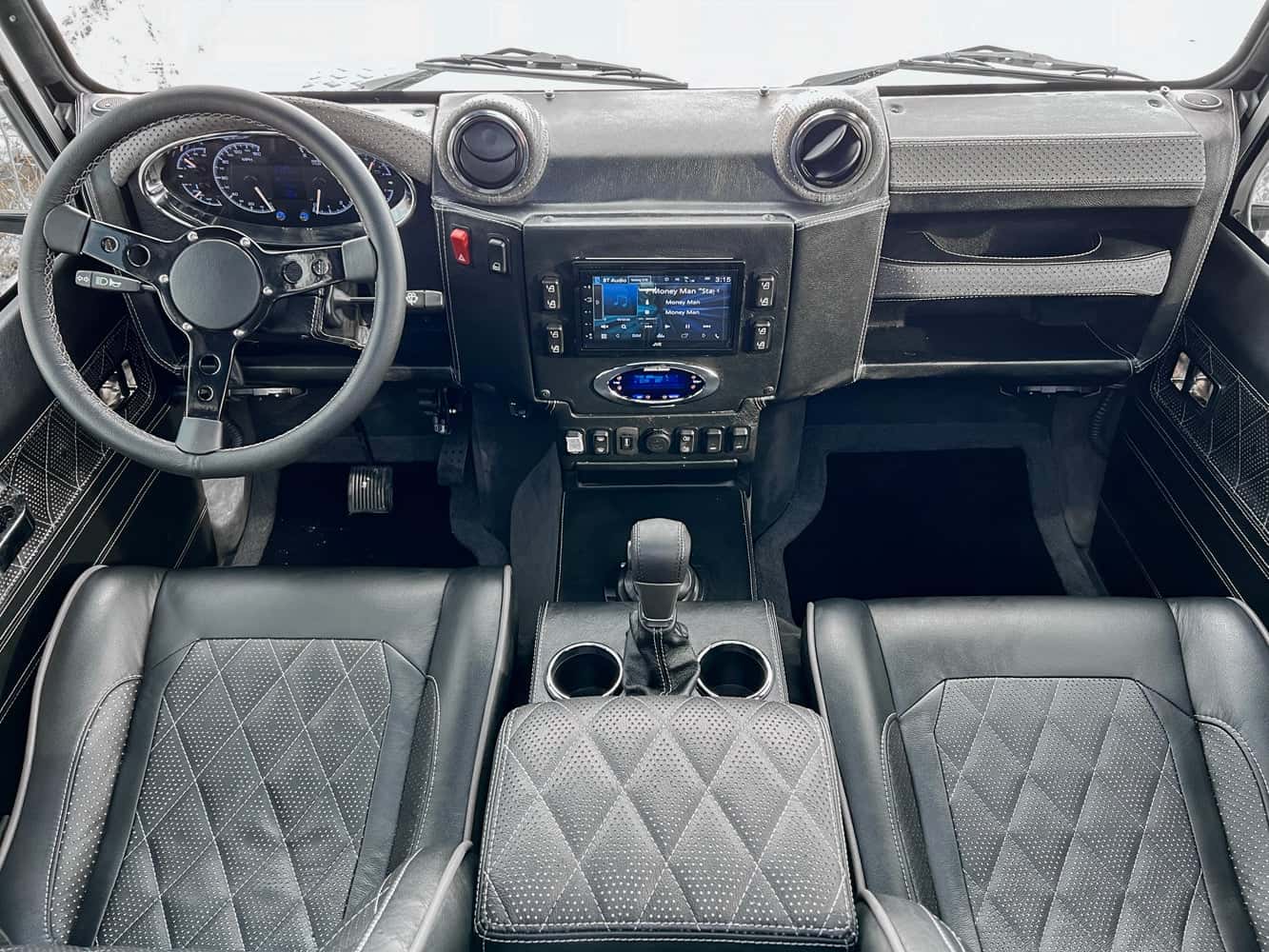 Interior view of a custom Land Rover Defender showcasing premium black leather seats and modern dashboard controls