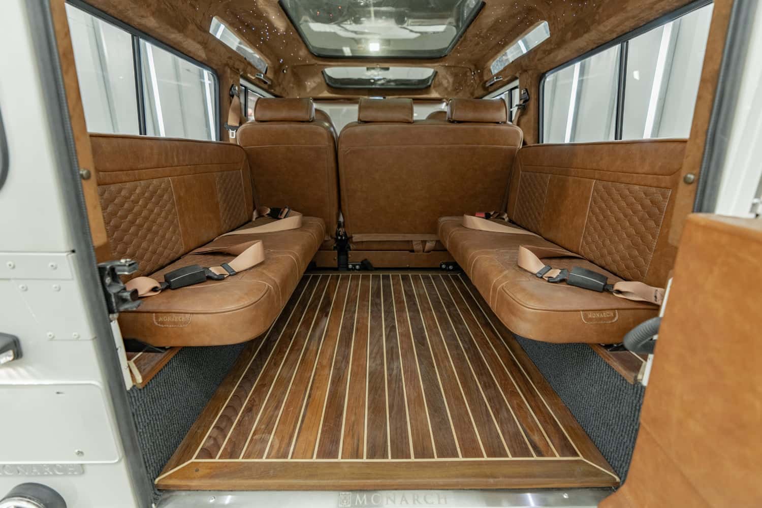 Interior view of a custom Land Rover Defender with luxurious brown leather seating and wooden flooring