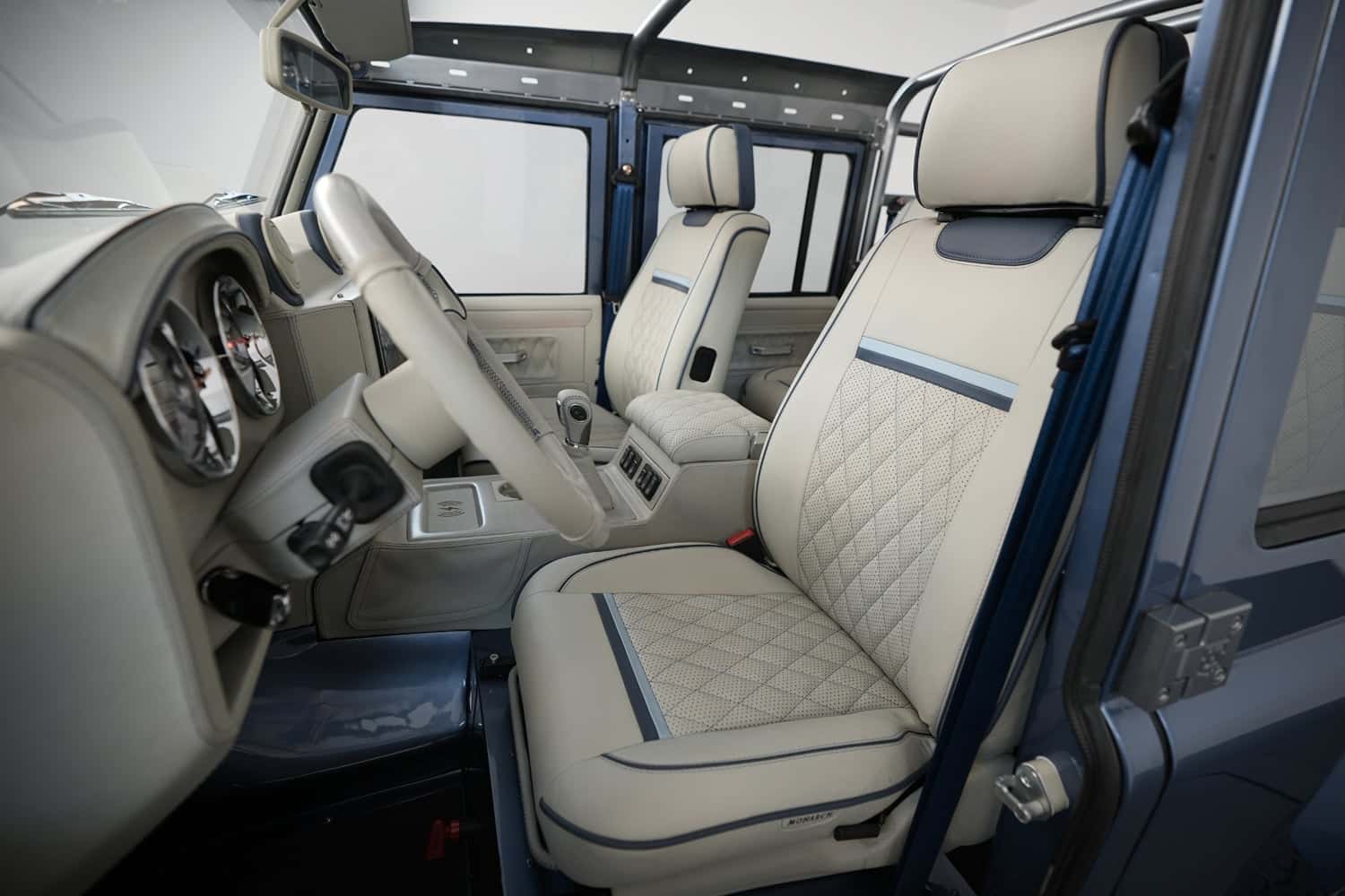 Interior view of a custom Land Rover Defender featuring premium beige leather seats with quilted design and modern dashboard.