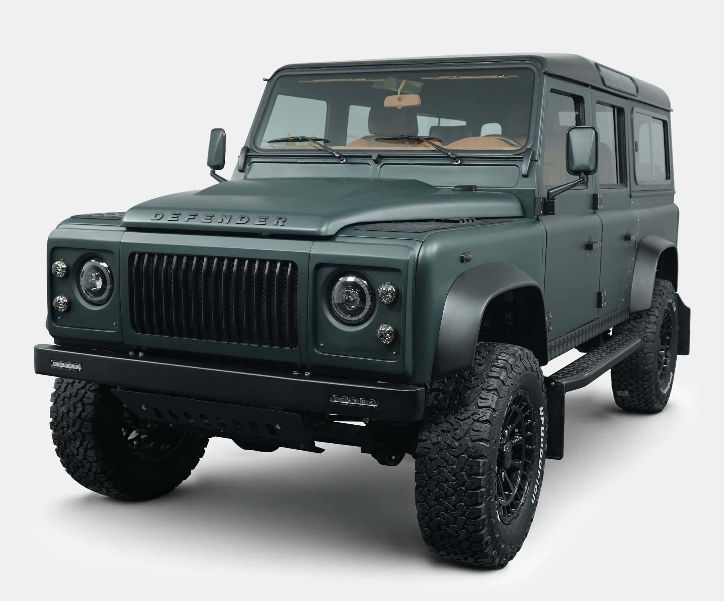 Front view of a custom Land Rover Defender in matte green finish with black accents and rugged tires