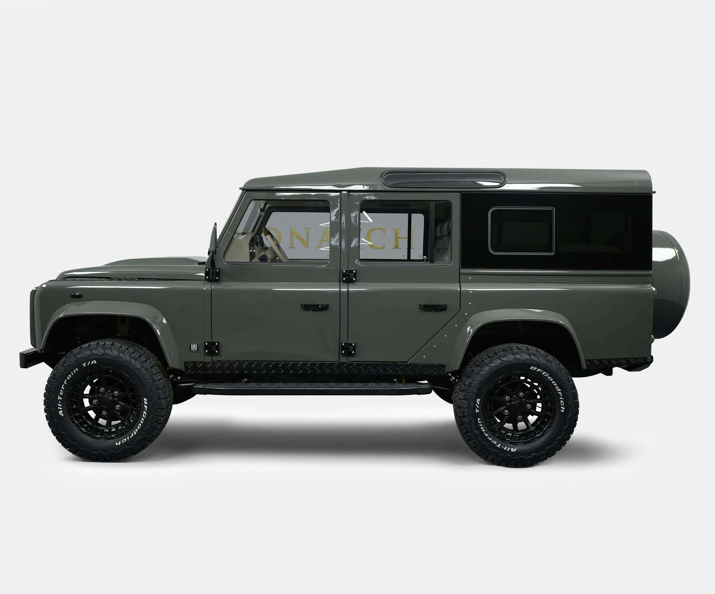 Side view of a custom Land Rover Defender in olive green with black accents and off-road tires