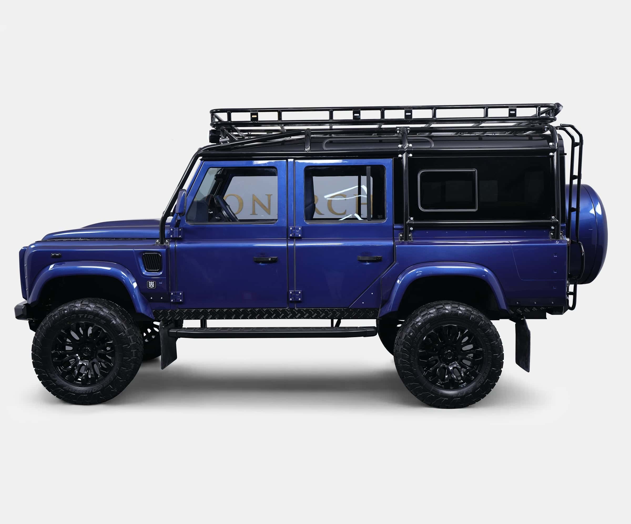 Side view of a bespoke blue Land Rover Defender with black alloy wheels and roof rack