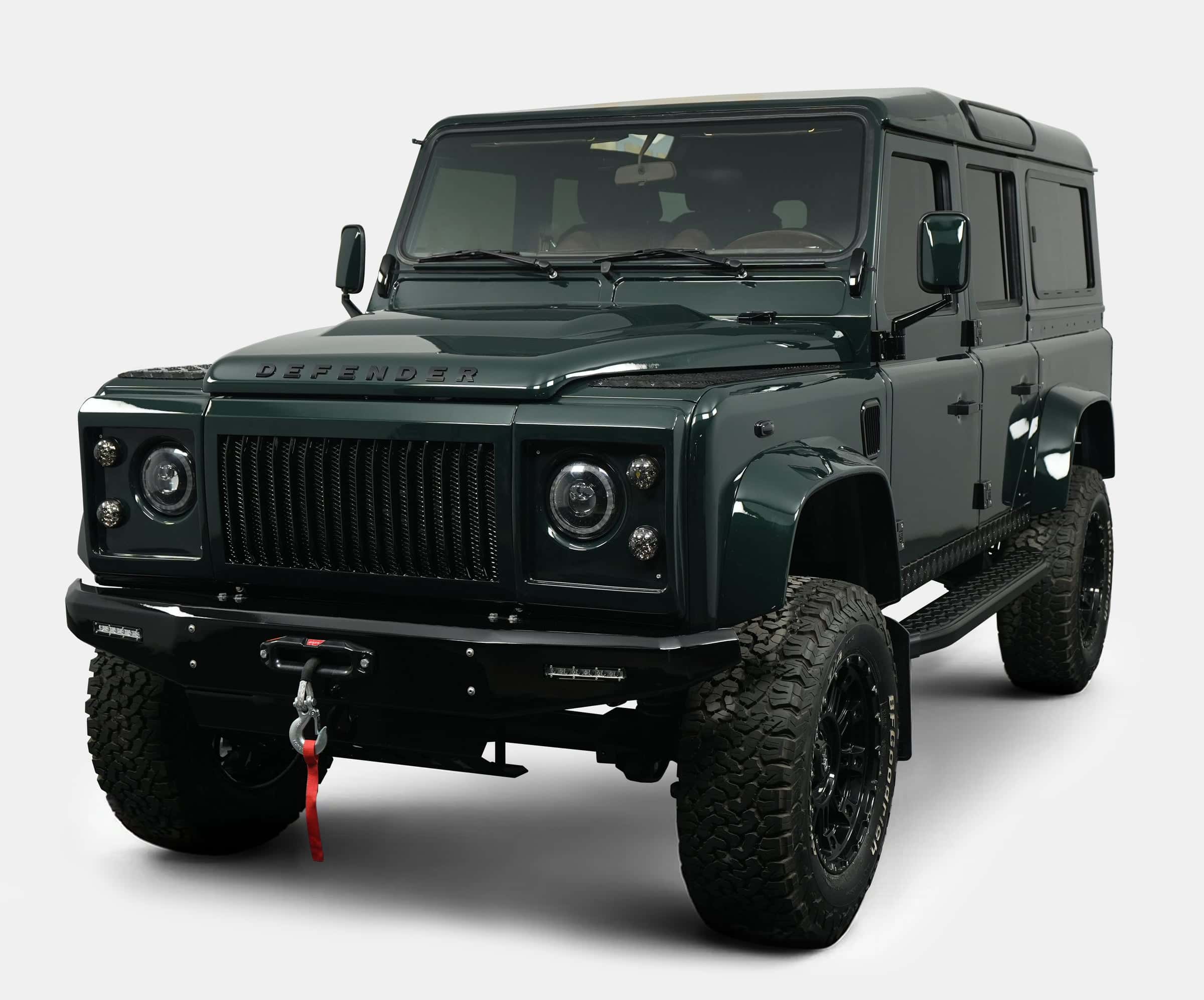 Front view of a custom Land Rover Defender in dark green with rugged tires and modern styling