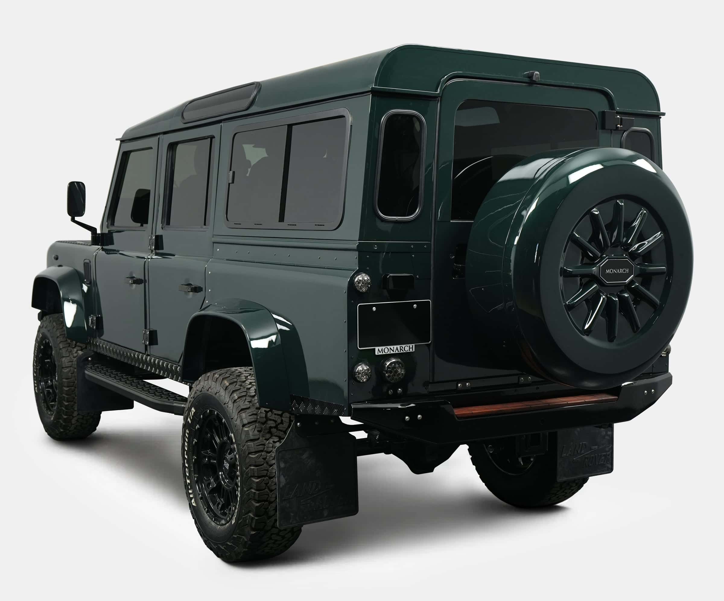 Rear view of a custom Land Rover Defender in dark green with a spare tire mounted on the back