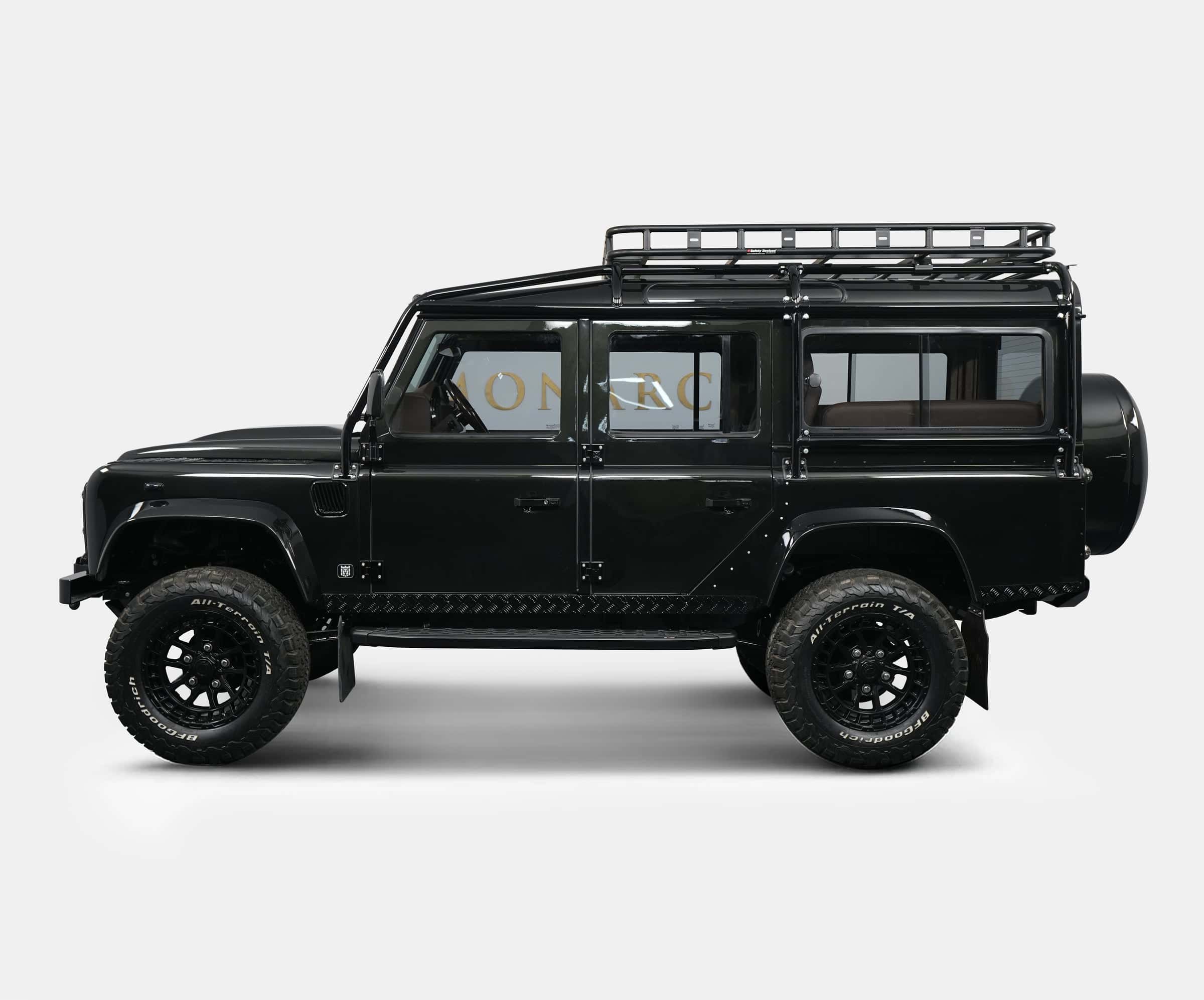 Side view of a bespoke black Land Rover Defender with off-road tires and a roof rack