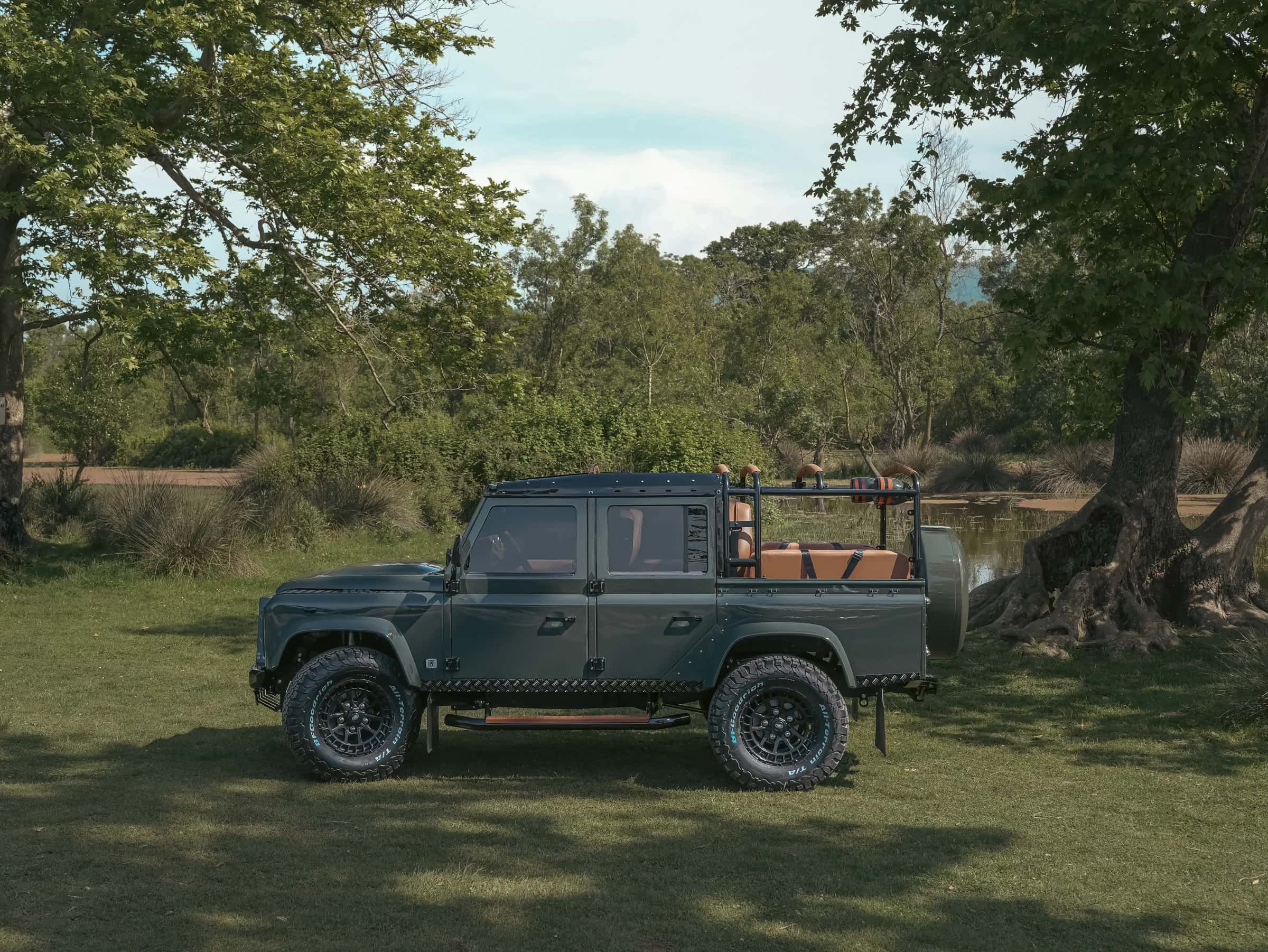Custom Land Rover Defender parked in a natural setting with green trees and water
