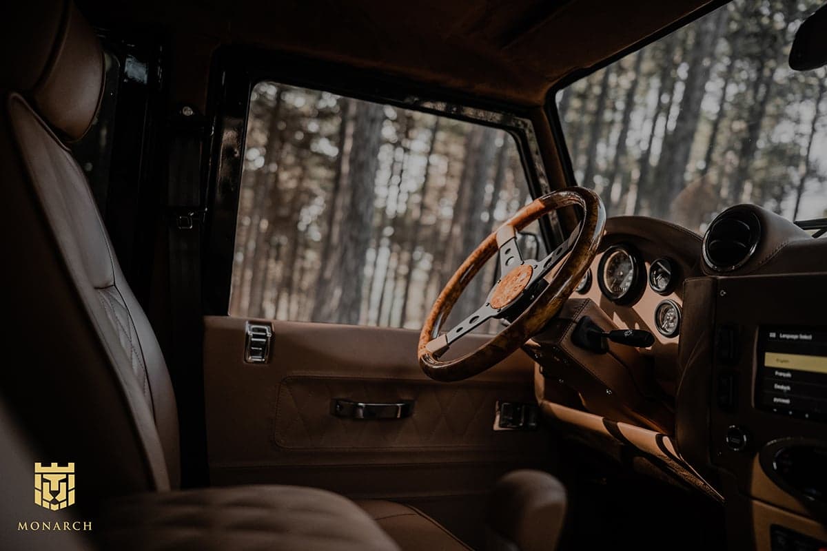 Interior view of a custom Land Rover Defender featuring a premium leather seat and wooden steering wheel