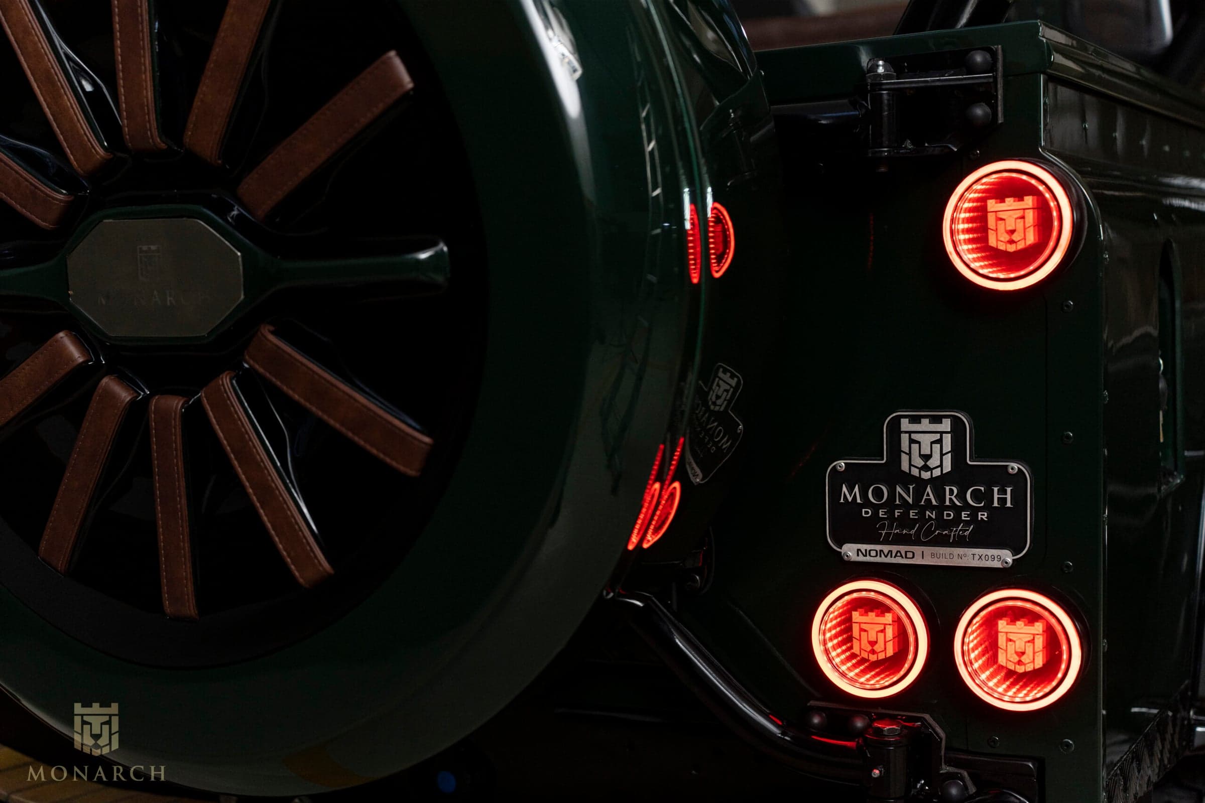 Close-up of a bespoke Land Rover Defender wheel with brown leather accents and illuminated tail lights