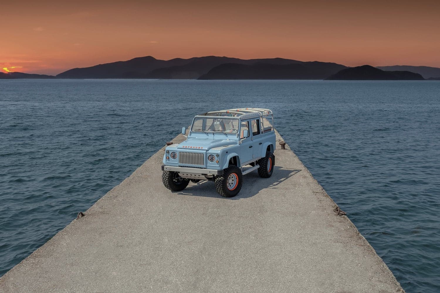Monarch Defender SUV on a pier at sunset with mountains in the background.