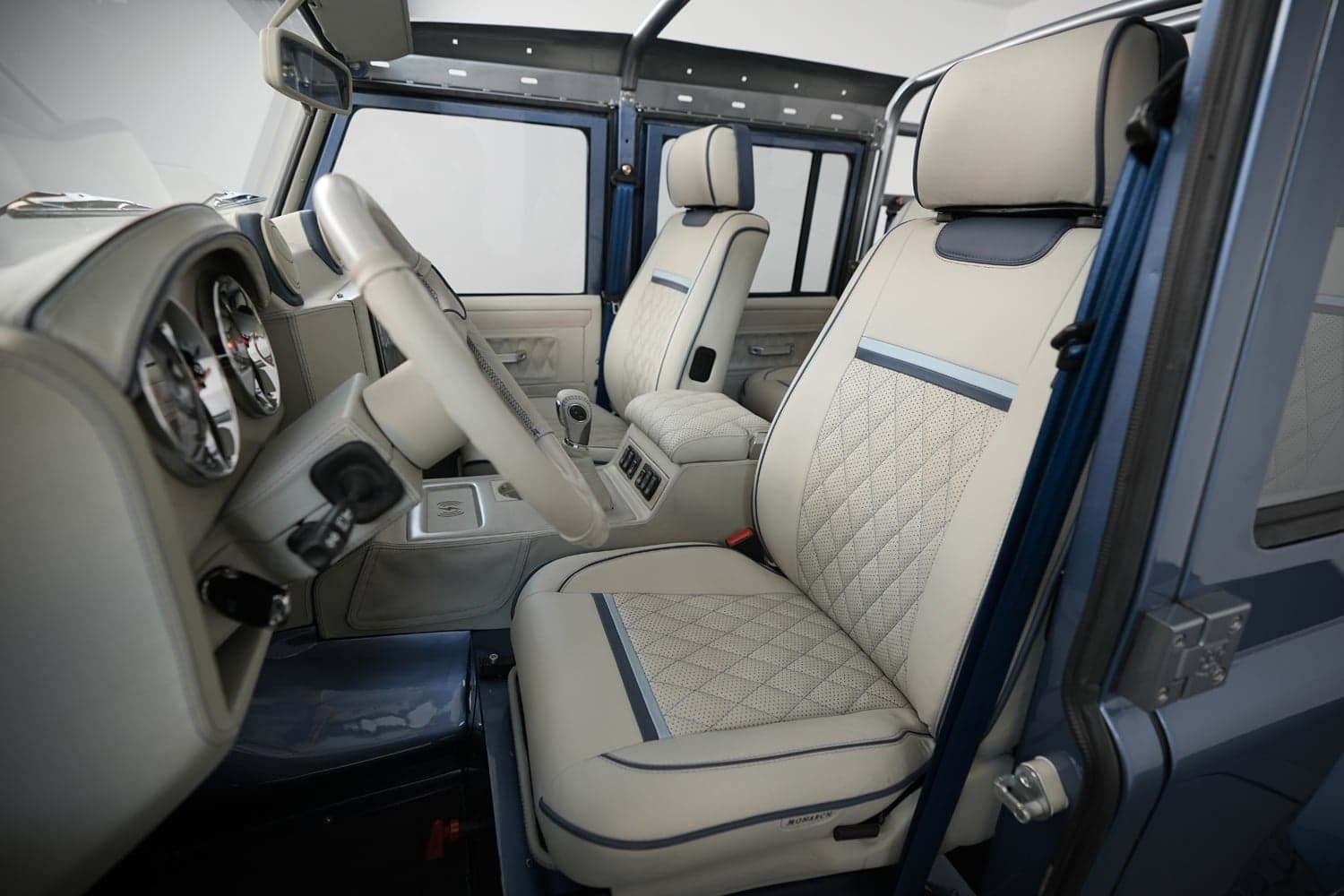 Interior view of a custom Land Rover Defender featuring premium beige leather seats with quilted design and modern dashboard.