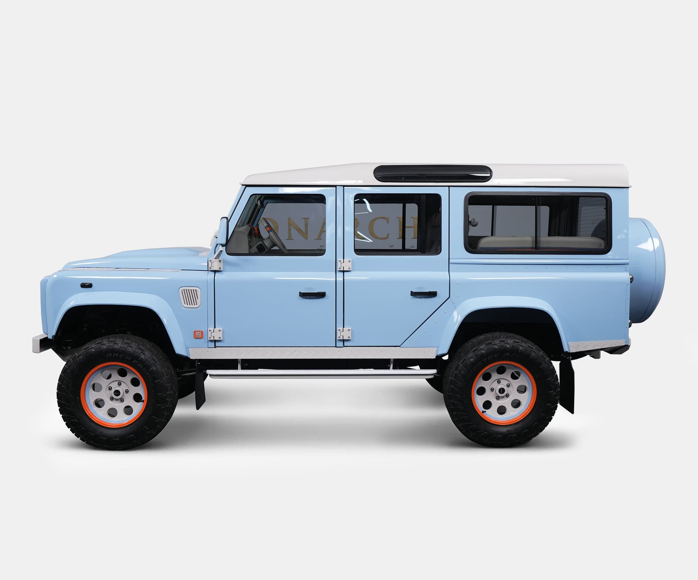 Side view of a bespoke Land Rover Defender in light blue with a white roof and orange accents