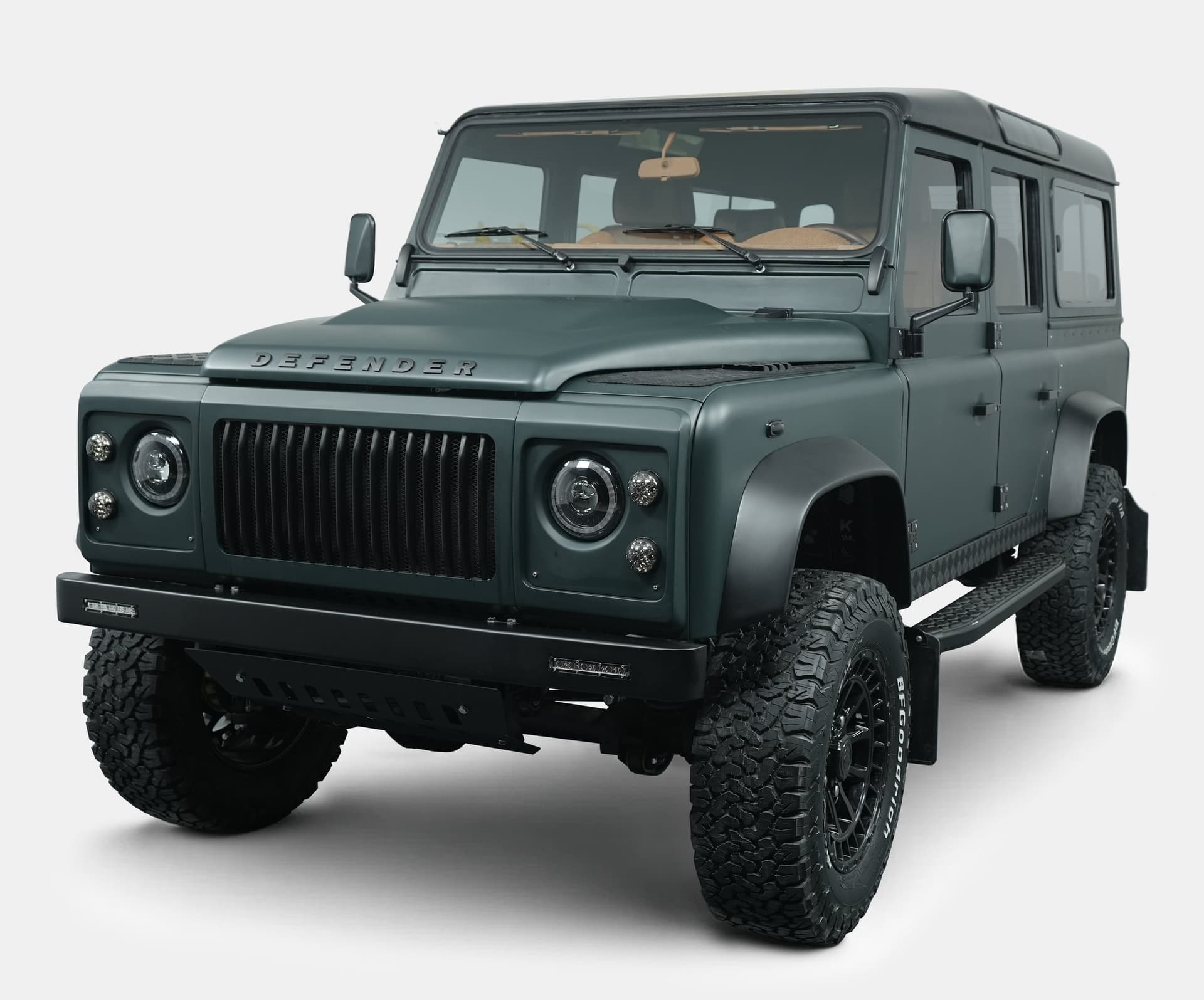 Front view of a custom Land Rover Defender in matte green finish with black accents and rugged tires