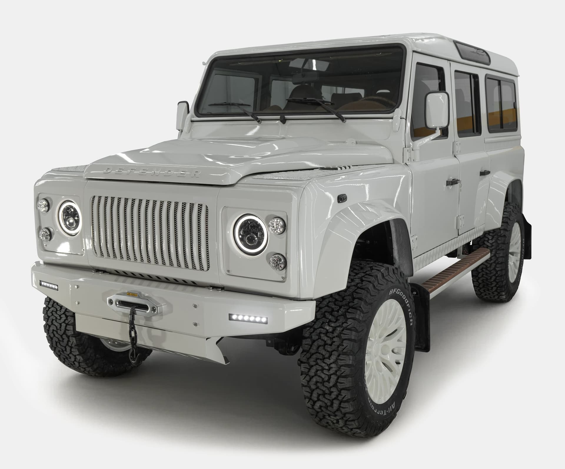 Front view of a custom Land Rover Defender in glossy white finish with modern headlights and rugged tires