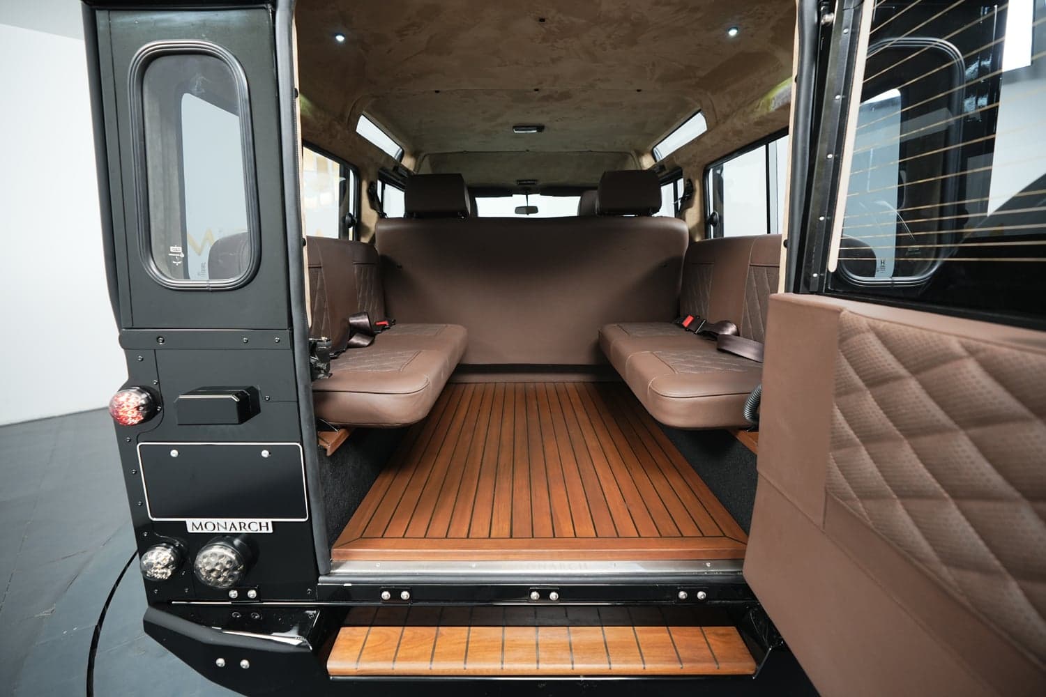 Interior view of a custom Land Rover Defender featuring brown leather seating and wooden flooring