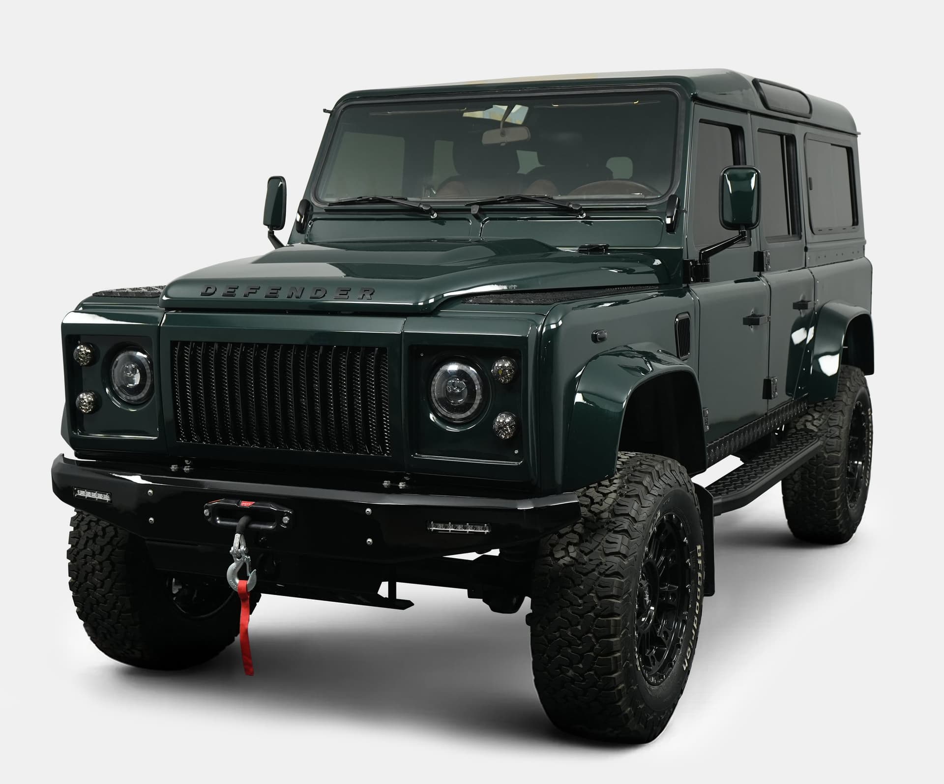 Front view of a custom Land Rover Defender in dark green with rugged tires and modern styling