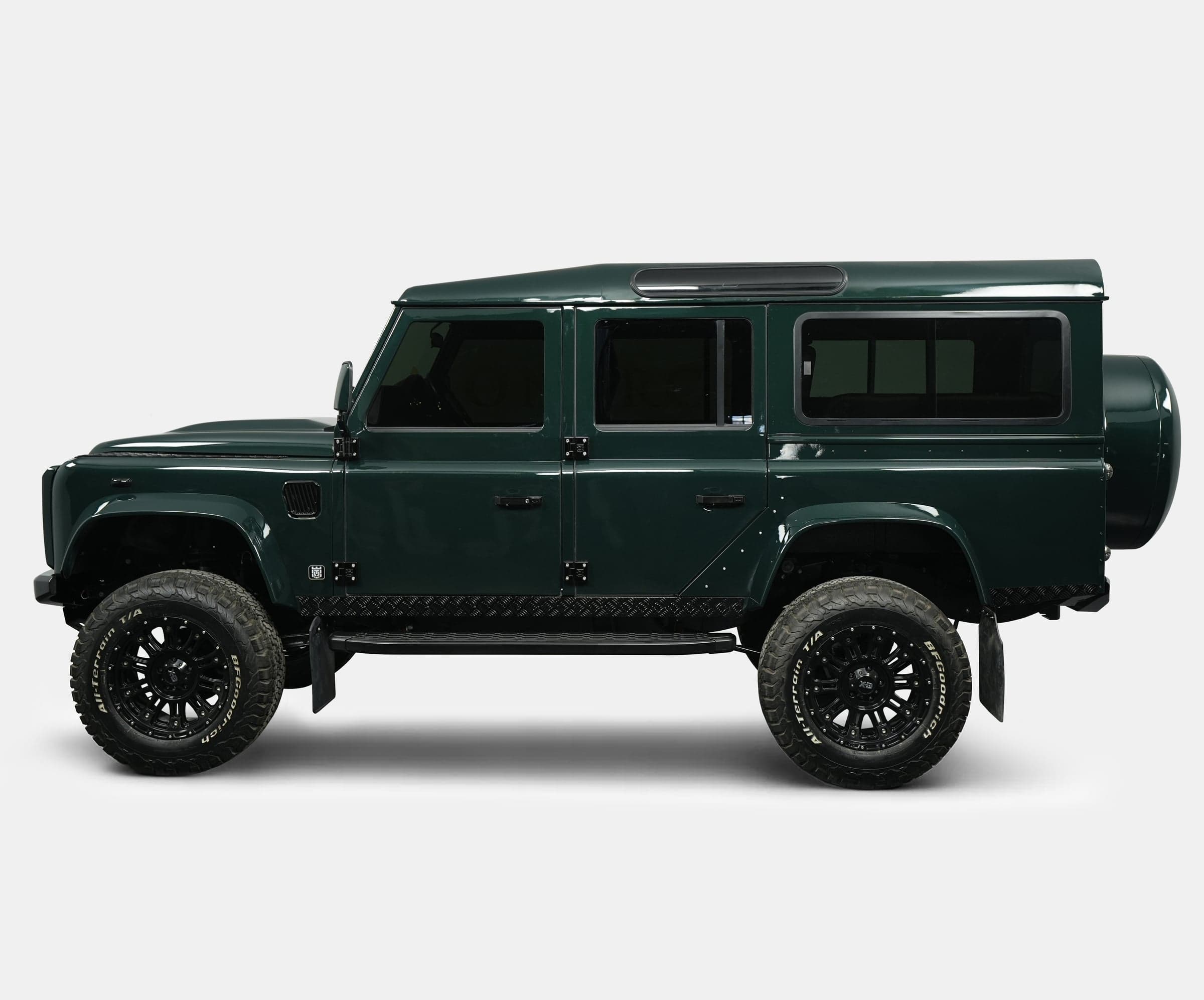 Side profile of a custom Land Rover Defender in dark green with black wheels