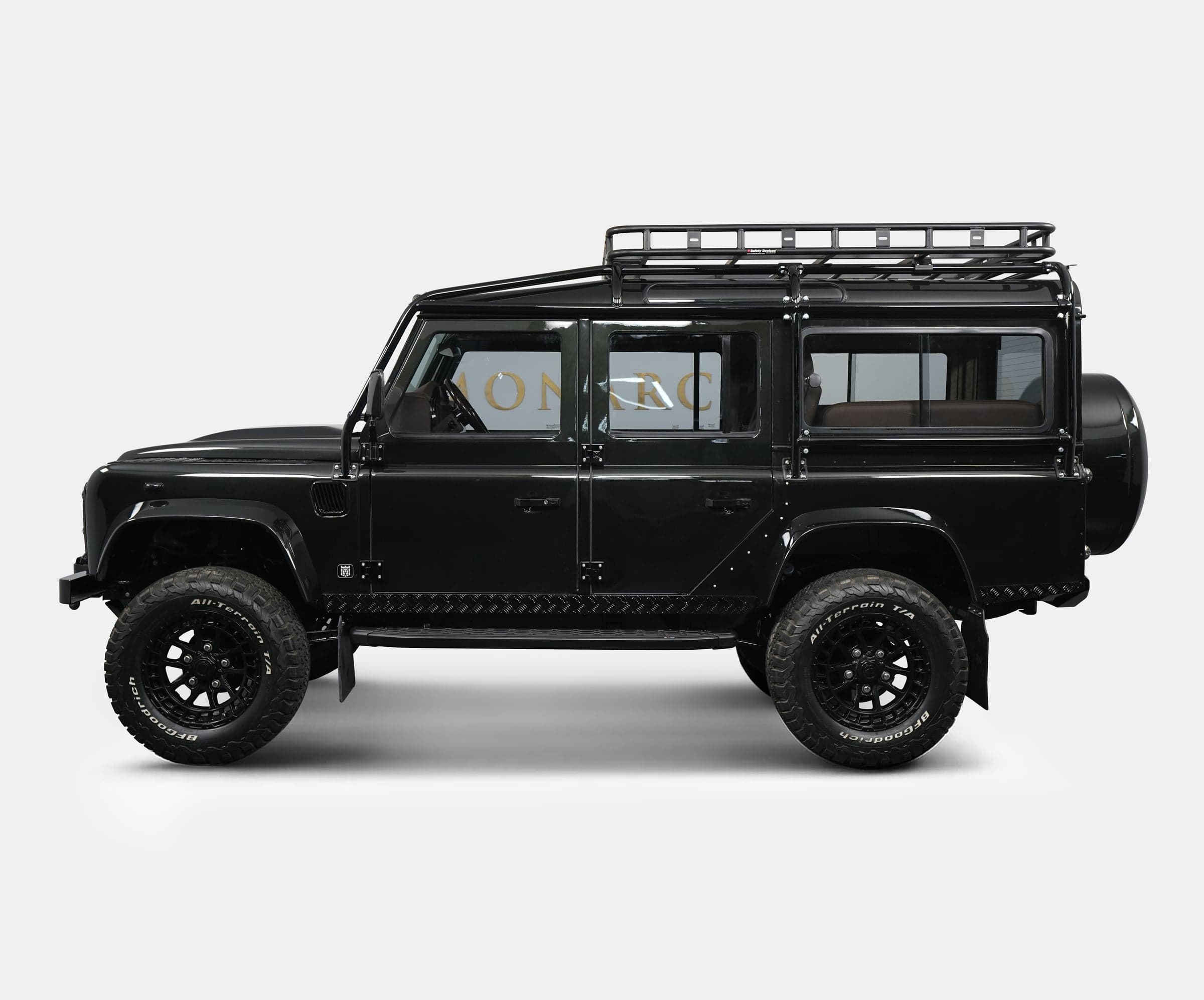 Side view of a bespoke black Land Rover Defender with off-road tires and a roof rack