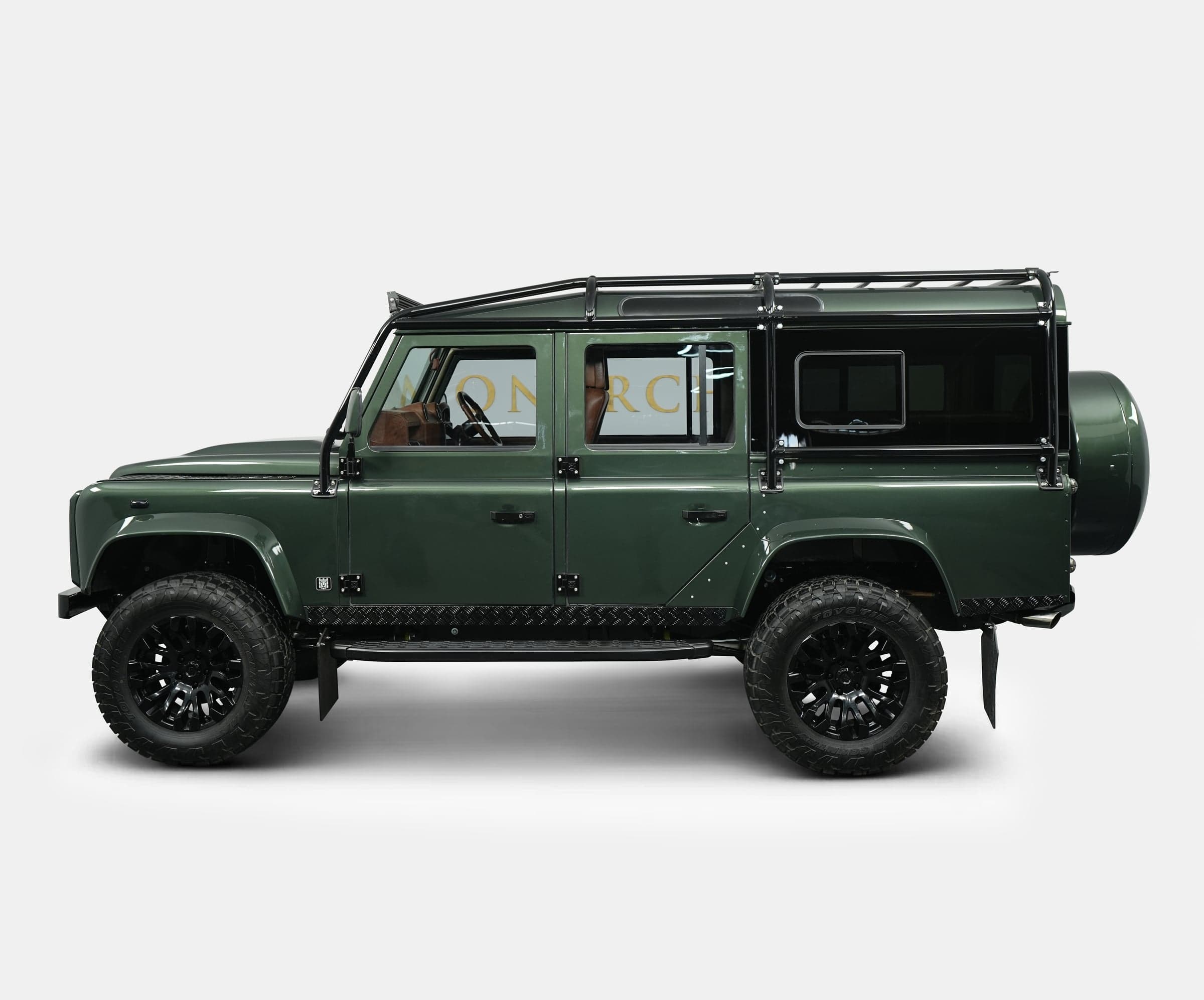Side view of a bespoke green Land Rover Defender with off-road tires and luxury details