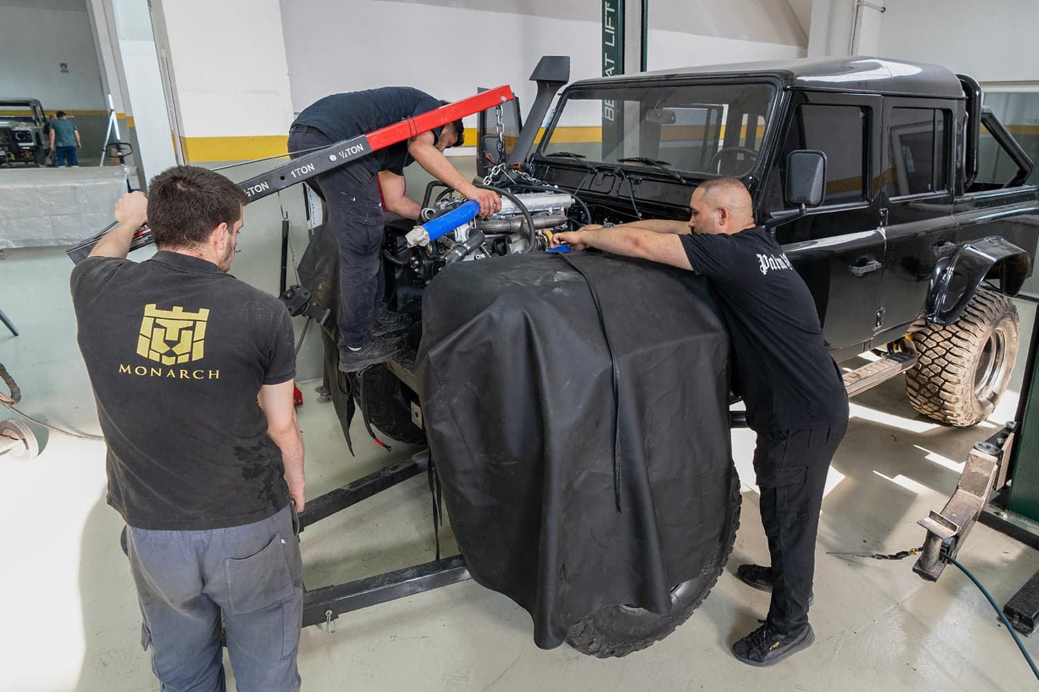Overhead view of a Monarch Defender build in progress, showing the galvanized chassis with modern drivetrain components being assembled during the 13-stage build process