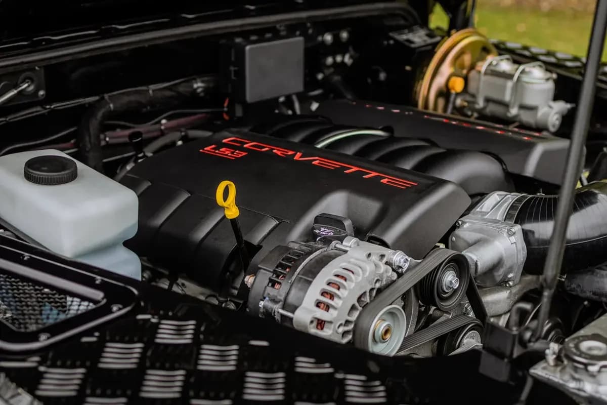 A classic Land Rover Defender 90 with its bonnet open, showing a freshly installed GM LS3 V8 engine in a clean engine bay with custom headers and polished intake