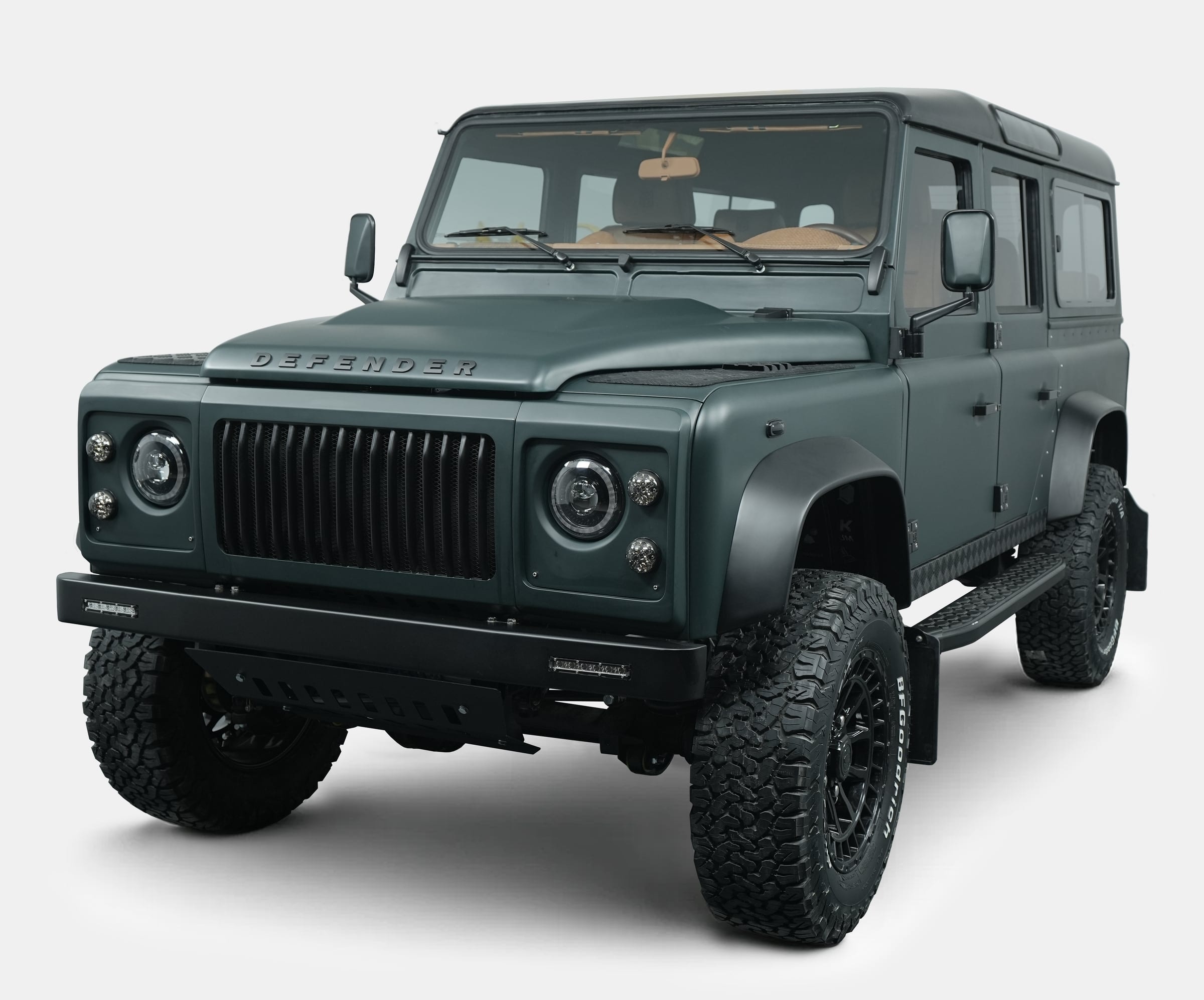 Front view of a custom Land Rover Defender in matte green finish with black accents and rugged tires