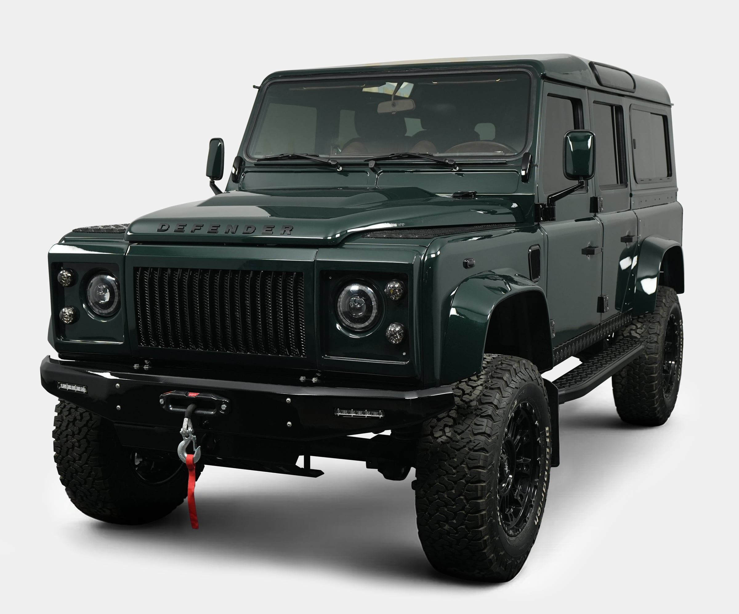 Front view of a custom Land Rover Defender in dark green with rugged tires and modern styling