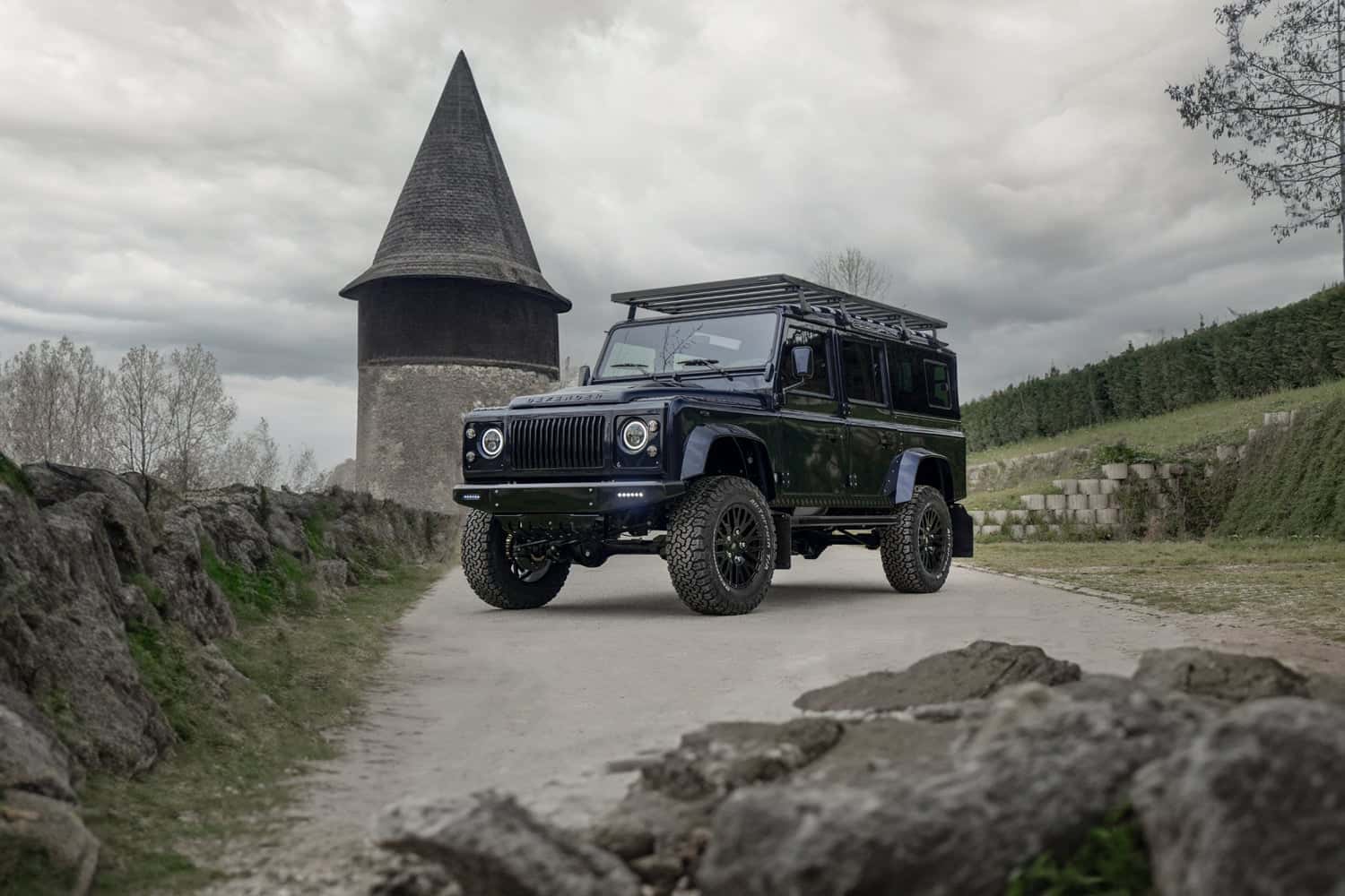 Front View: Custom Land Rover Defender Modified Land Rover Defender parked on a gravel path near a historic tower