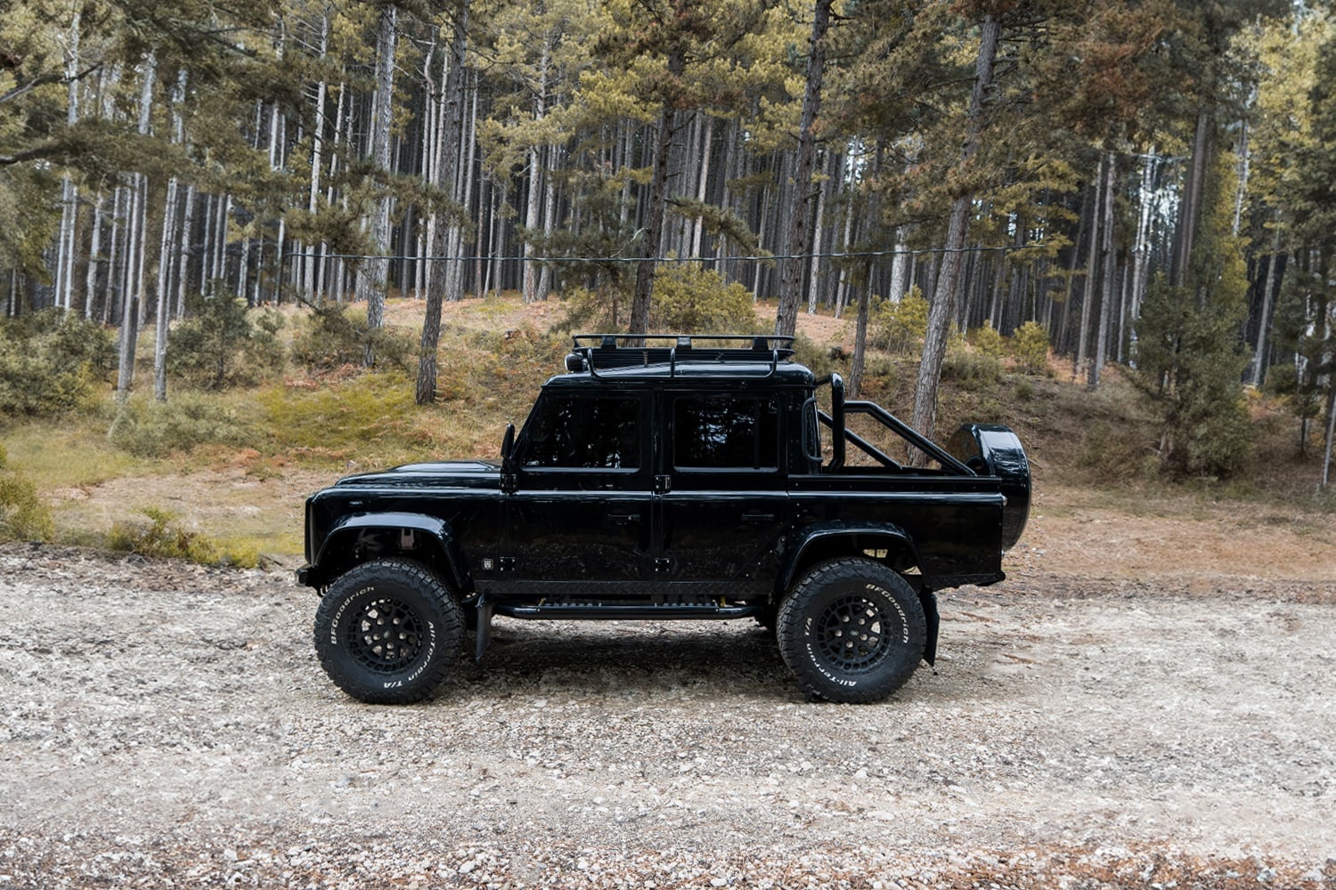 Side View: Custom Black Defender Side view of a custom black Land Rover Defender parked in a forest setting