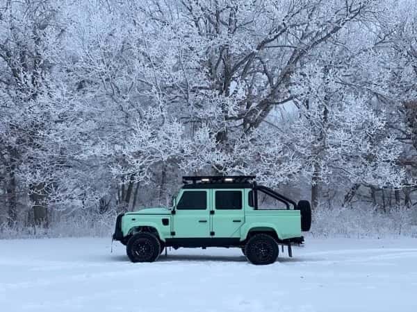 Side View: Custom Land Rover Defender A mint green custom Land Rover Defender parked in a snowy landscape with frosted trees in the background