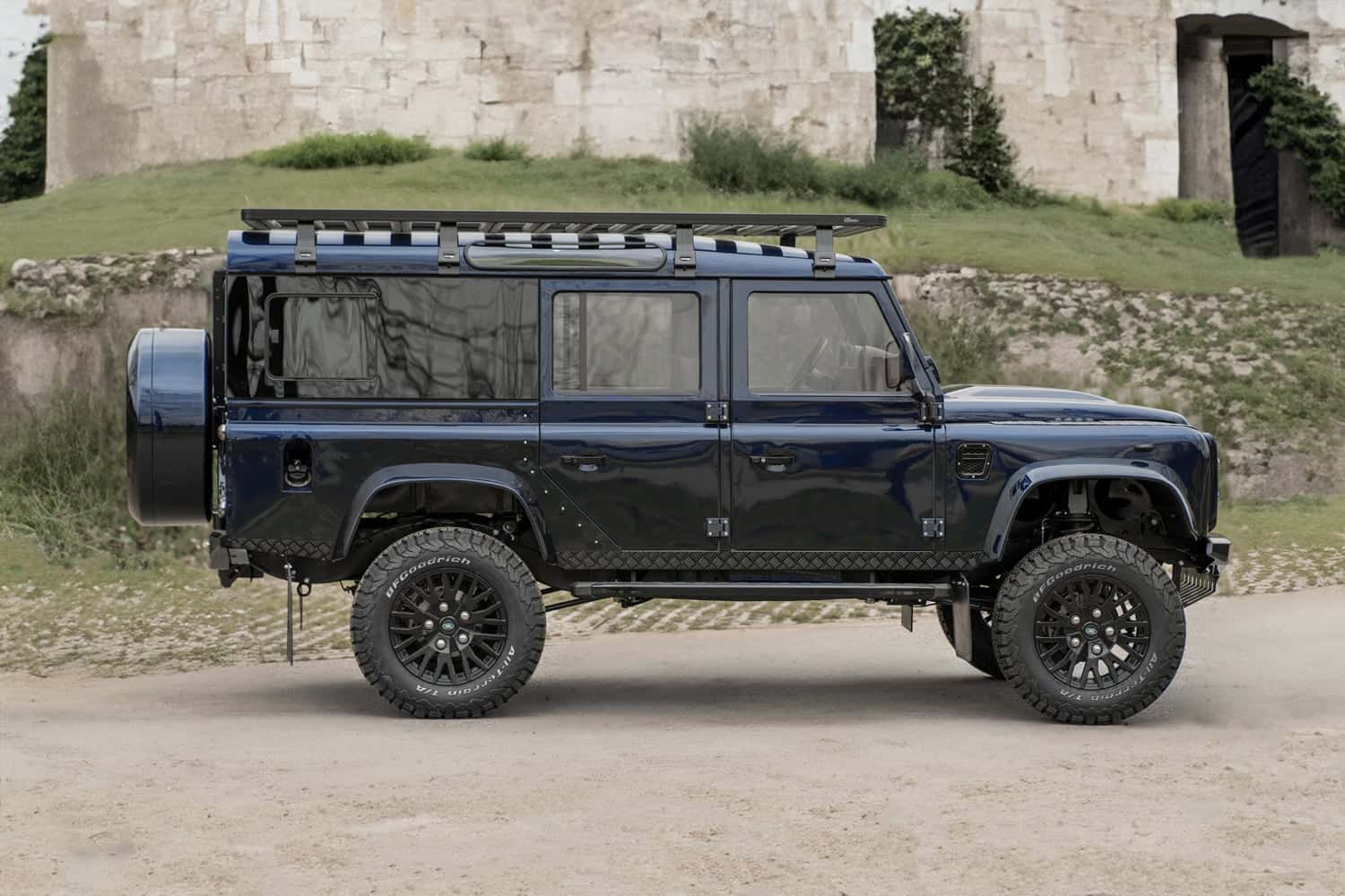 Side View: Bespoke Land Rover Defender Custom blue Land Rover Defender parked on dirt with rugged terrain