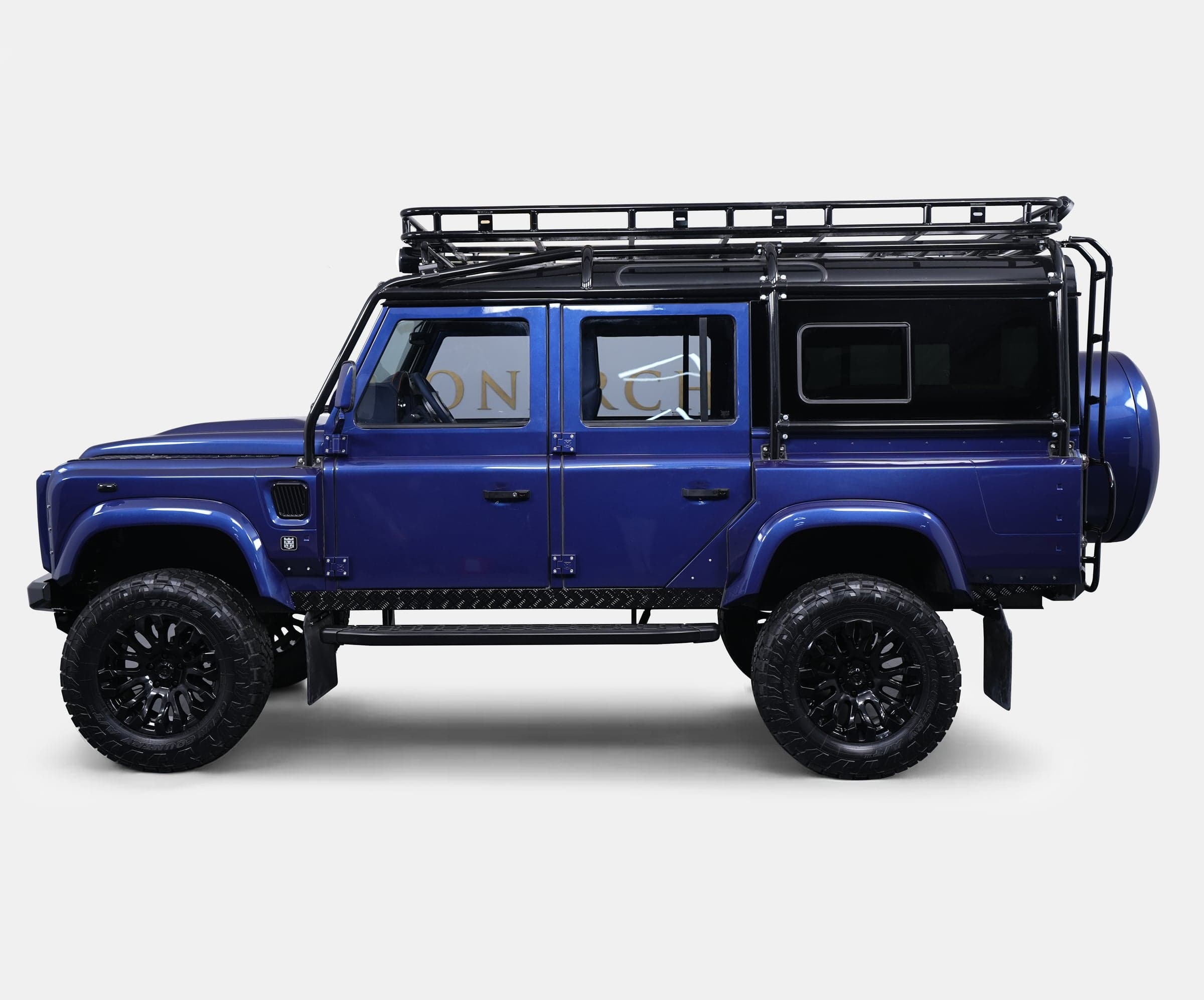 Side View: Custom Land Rover Defender Side view of a bespoke blue Land Rover Defender with black alloy wheels and roof rack