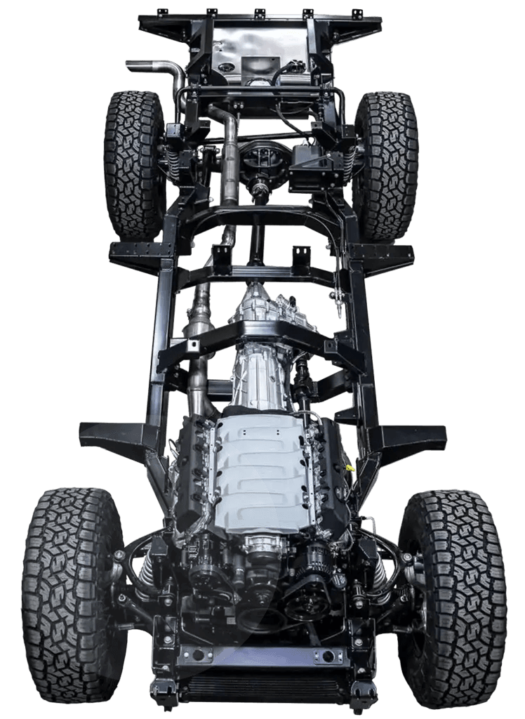 A stripped and galvanized Defender chassis on a build stand in a workshop, gleaming zinc finish visible on all surfaces, with the body removed