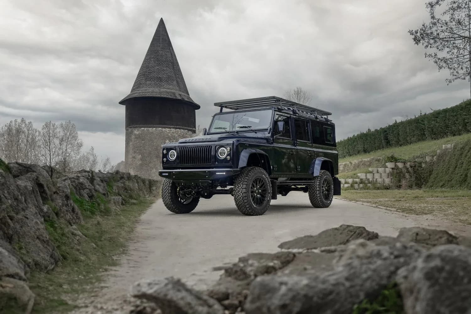 A pristine vintage Land Rover Defender 90 in Coniston Green, shot from a three-quarter front angle on a gravel road with rolling countryside behind it