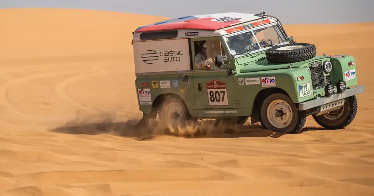 A classic Defender's front side, with event stickers and badges from various Land Rover rallies on the windshield