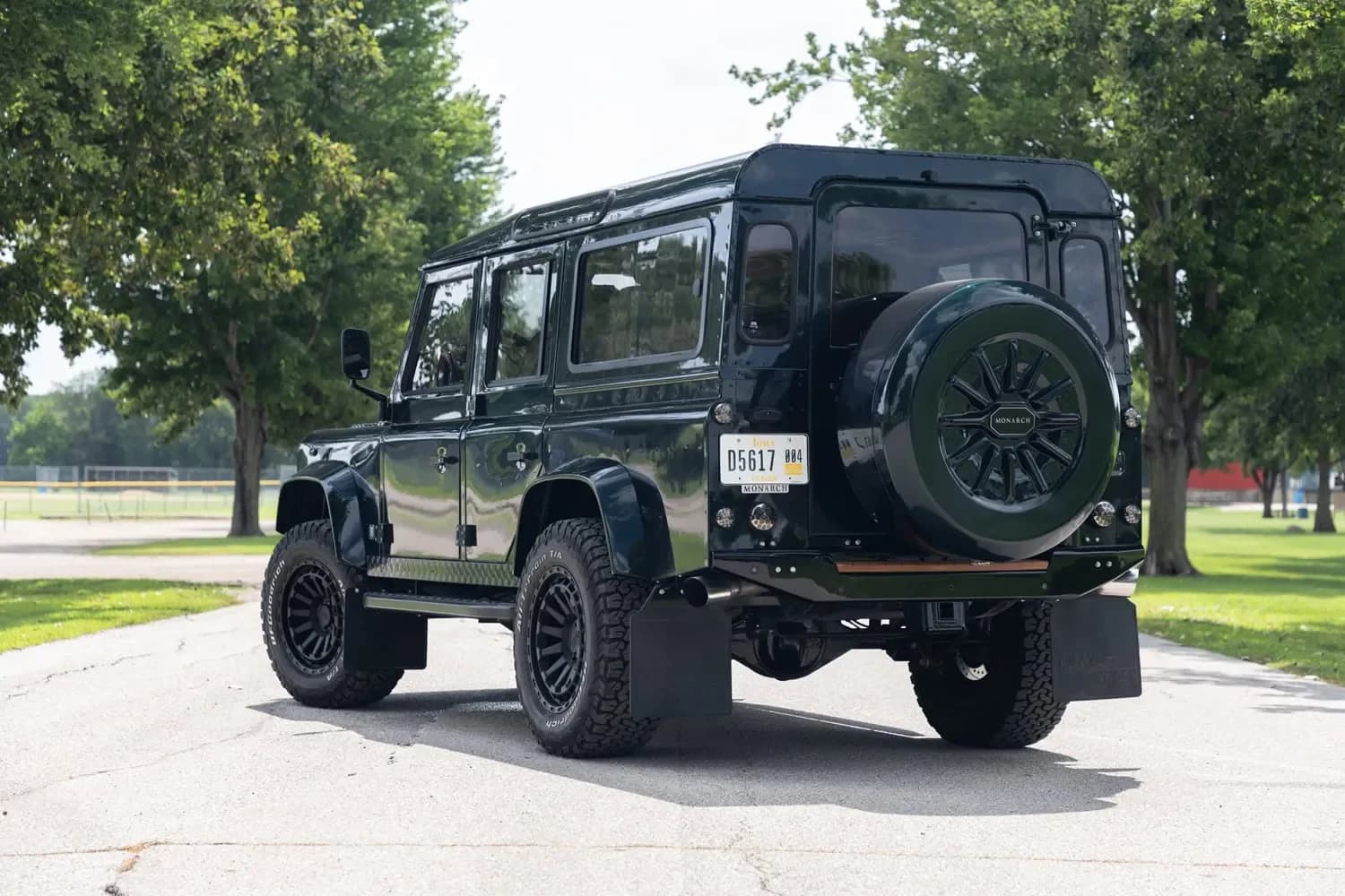 Finished custom Defender 110 in a deep heritage green, photographed at golden hour on a rural road, showing the profile with upgraded wheels and subtle stance improvements