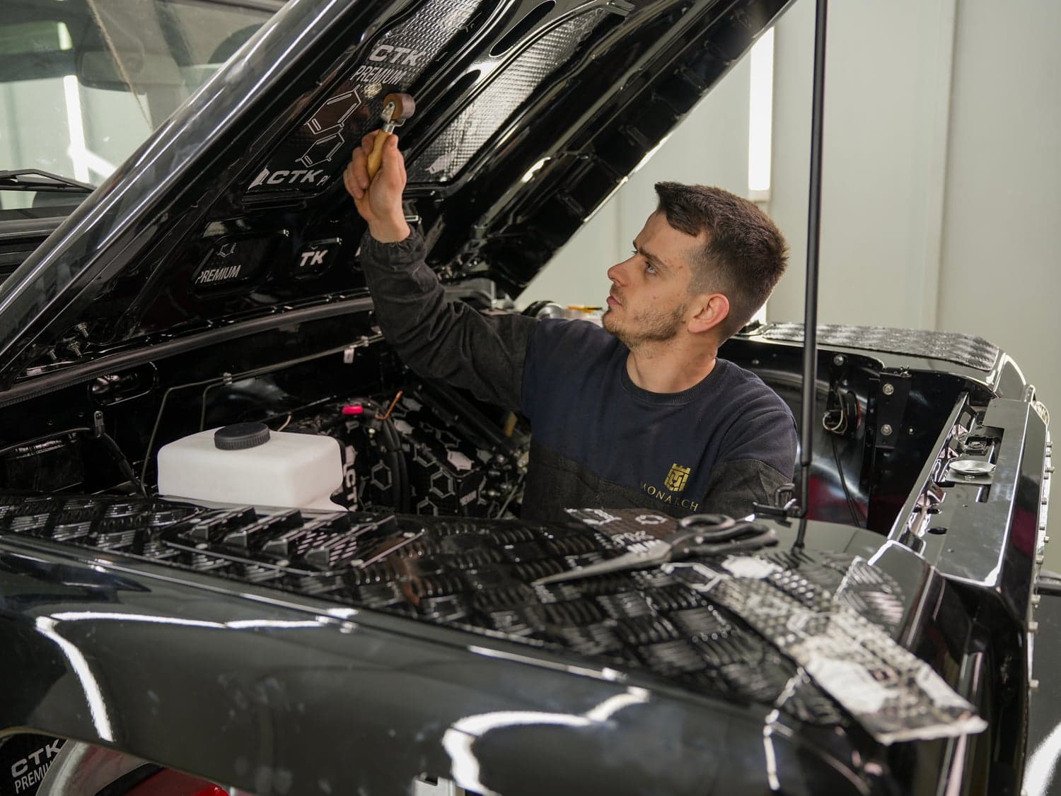 A classic Defender 110 in the final assembly stage of a ground-up build, showing the bare galvanized chassis with the LS3 V8 engine installed, in a professional workshop setting