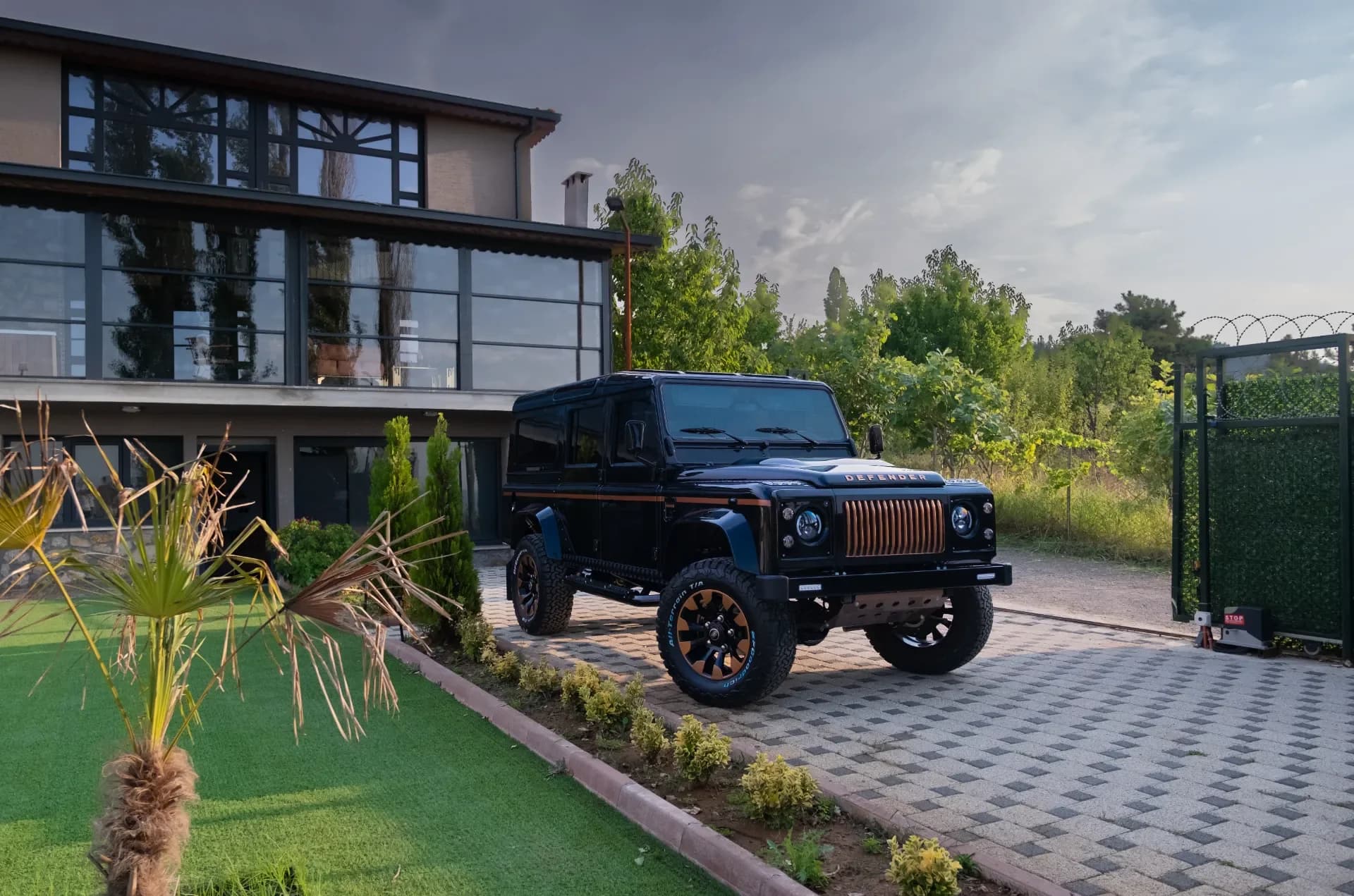 A finished bespoke Defender 90 in a custom color, parked in a scenic location, showcasing the completed build with premium wheels, upgraded lighting, and professional paint finish