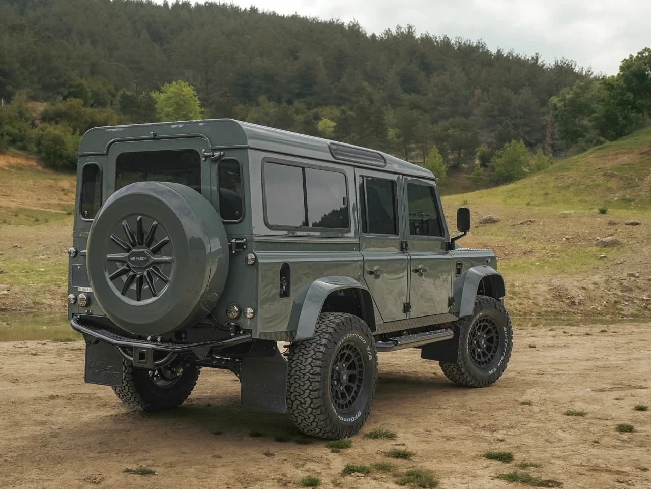 Bespoke Land Rover Defender in green color with custom wheels parked in a natural setting